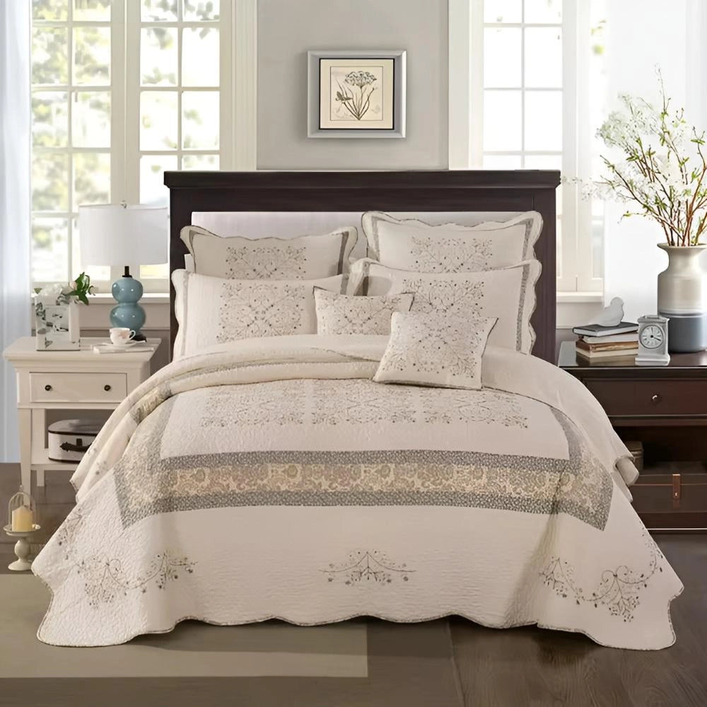 Luxury floral quilt set featuring embroidered pillowcase and scalloped edges on a neatly made bed with a wooden bed frame, set in a comfortable and stylish interior with a window, picture frames, and decorative plants.
