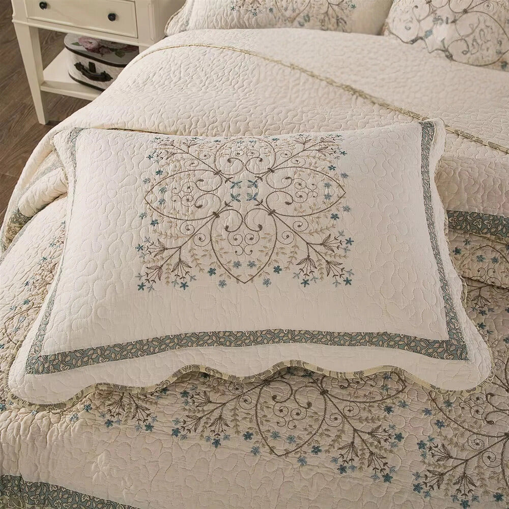 Luxury floral quilt set featuring embroidered pillowcase with scalloped edges, displayed on a beige background, showcasing intricate motifs and embellishments.