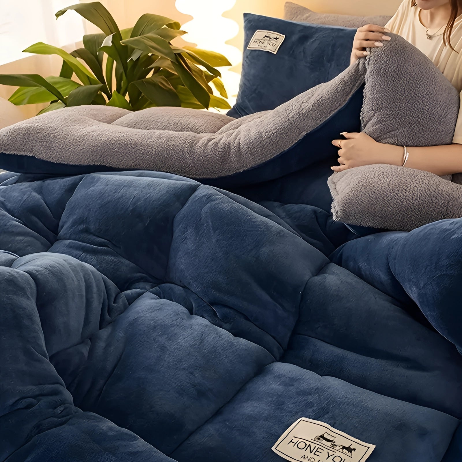 A luxurious gray velvet blanket draped over a couch, showcasing its premium soft texture suitable for winter comfort. The setting includes a cozy atmosphere with a glimpse of a plant in the background.