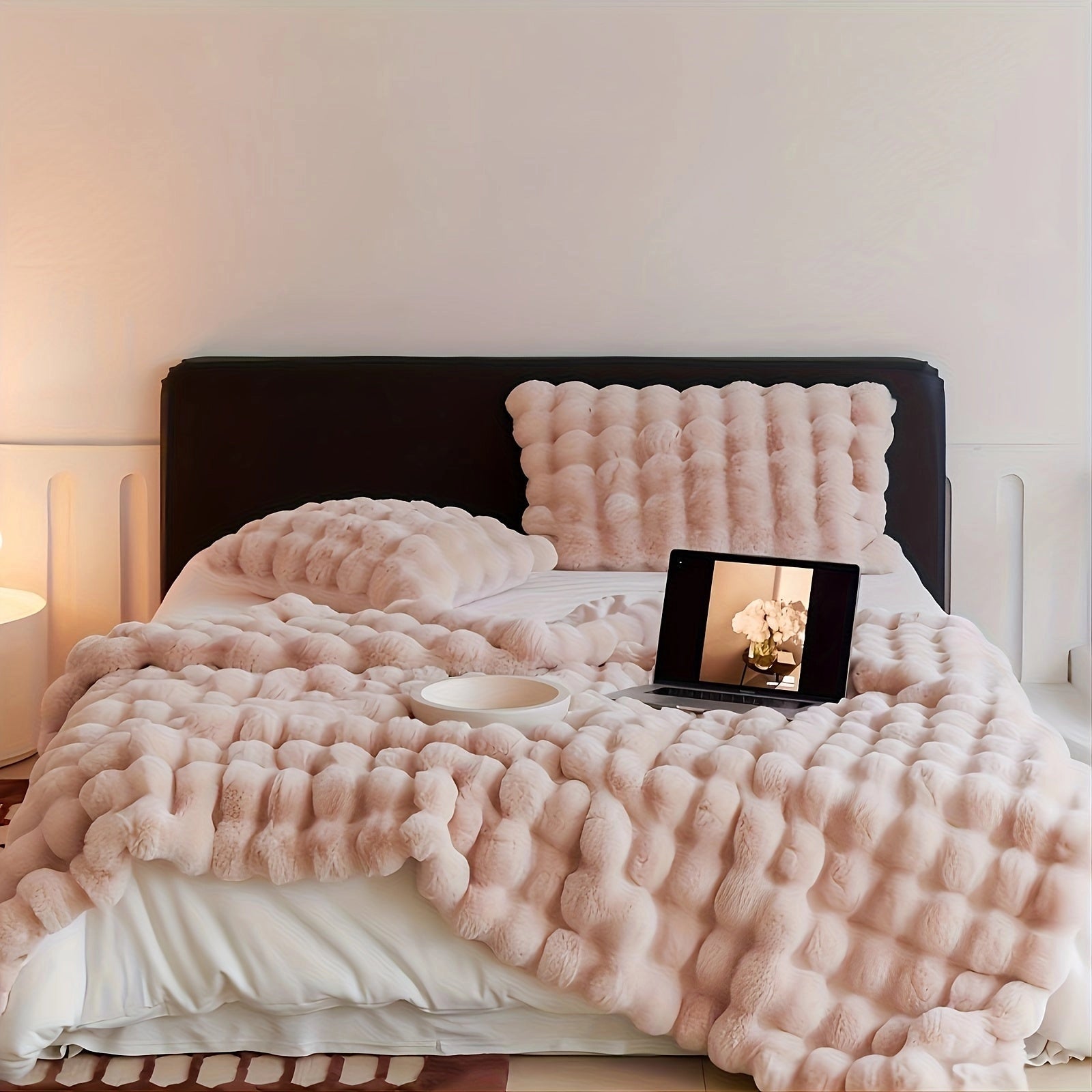 Luxurious oversized faux fur blanket in plush soft pink, draped over a couch in a cozy setting, with pillows and wooden furniture in the background.