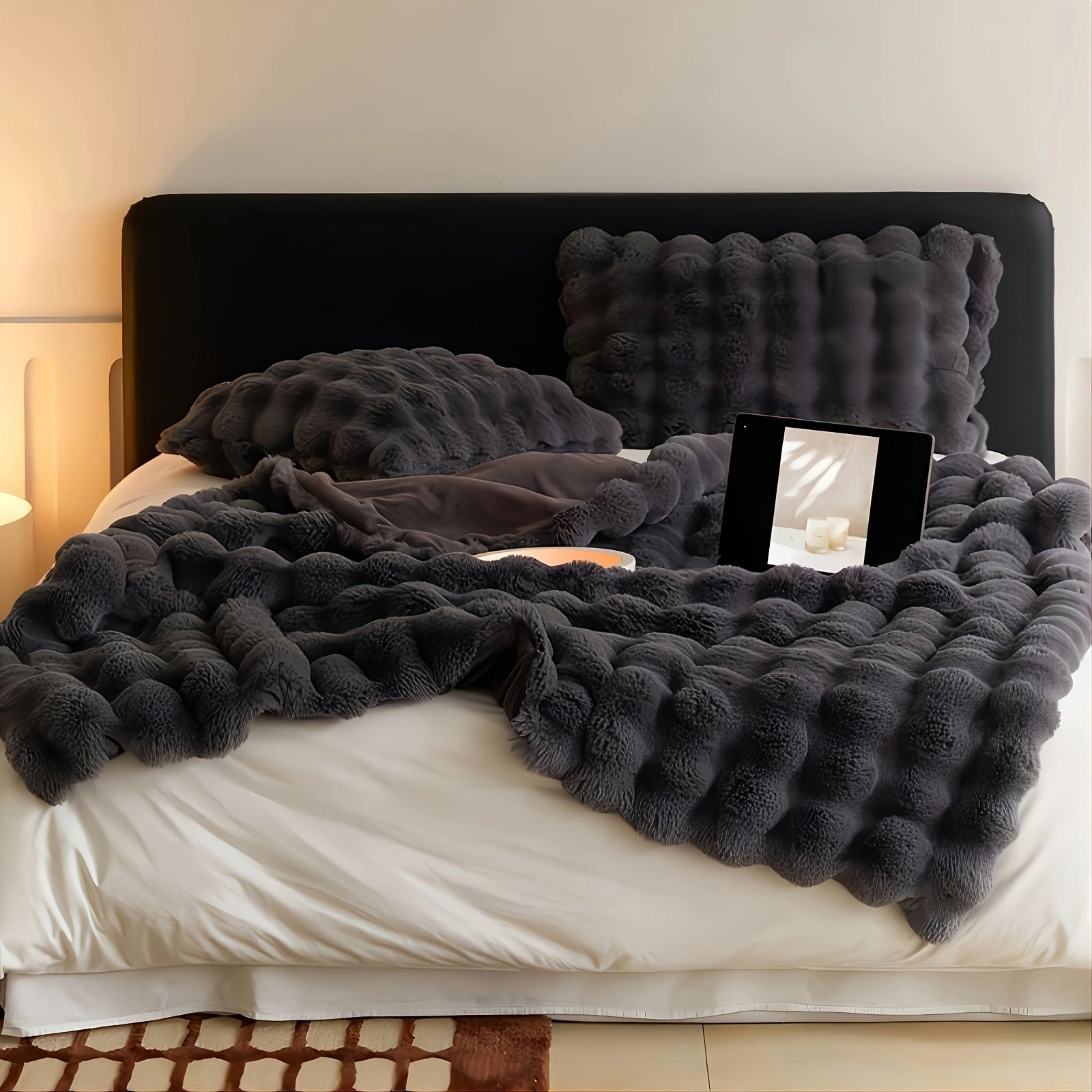 Gray luxury oversized faux fur blanket draped over a studio couch, highlighting its plush texture and soft textile design. The background features elements of wood and hardwood flooring, accentuating the cozy and elegant atmosphere.
