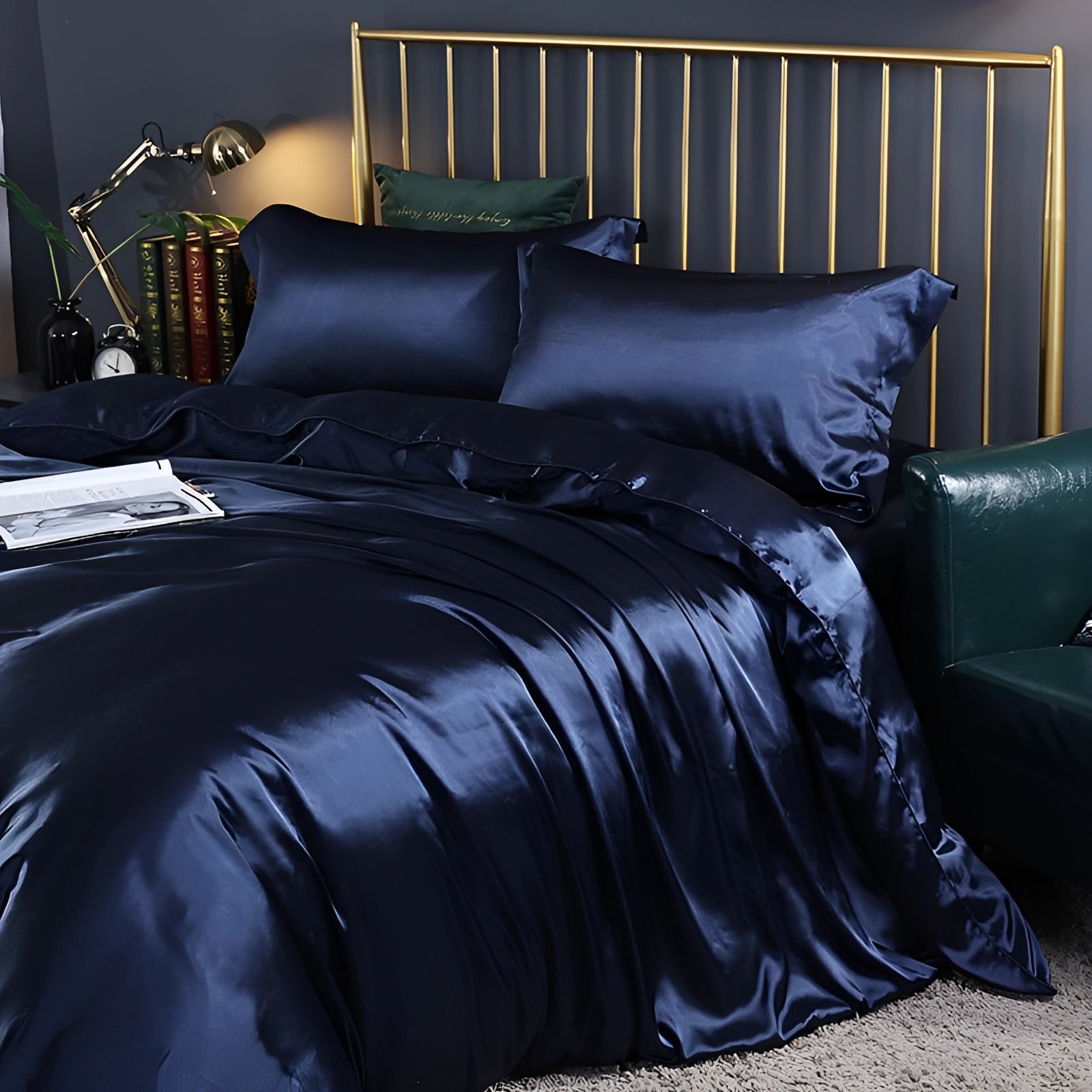 Luxury dark blue silk bedding set with a hypoallergenic and thermal regulating design, featuring a fitted sheet, displayed on a wooden bed frame with matching pillows in a cozy, warmly lit bedroom.