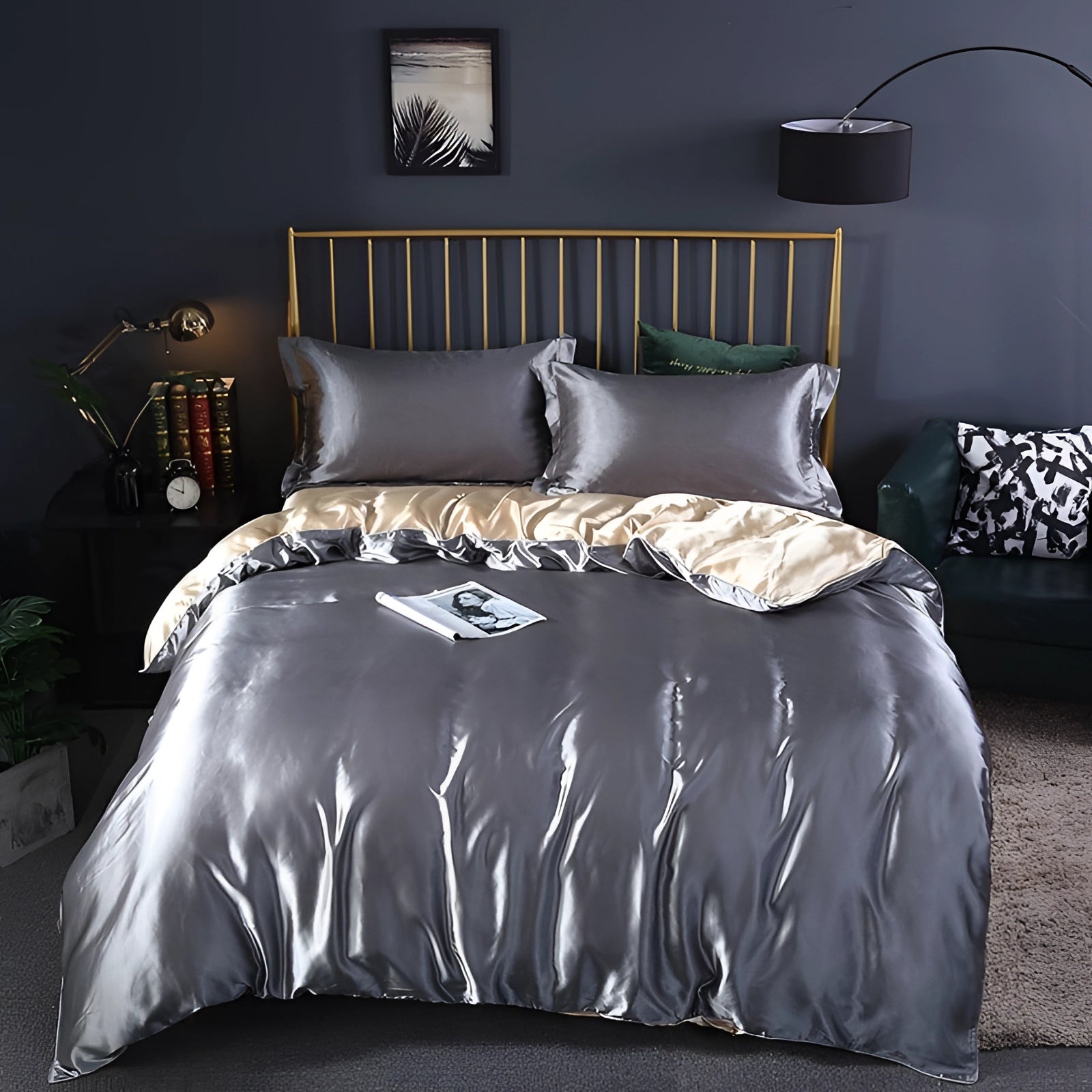 Luxury silk bedding set in metallic silver tones displayed on a neatly made bed, featuring a fitted sheet, pillowcases, and duvet cover in a 180x200cm size. The bed is part of a well-designed interior with a wooden bed frame, ambient lighting from a nearby lamp, and a window allowing natural light, all contributing to a comfortable and elegant atmosphere.