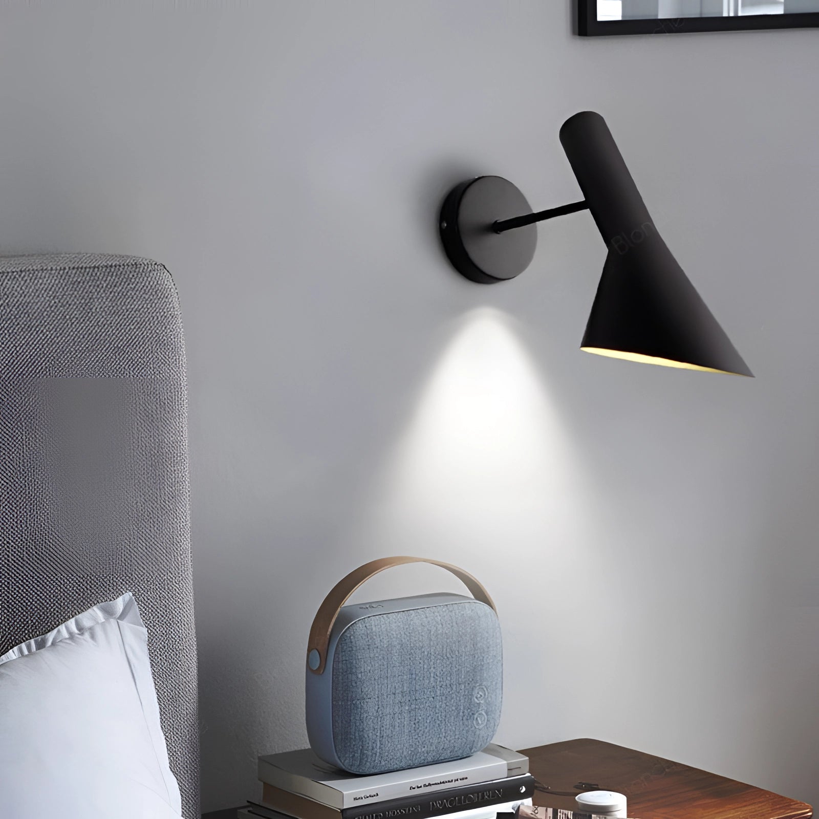 Matte black adjustable LED wall lamp mounted on a grey and wood interior wall, illuminating a modern bedroom setting with stylish and functional lighting.
