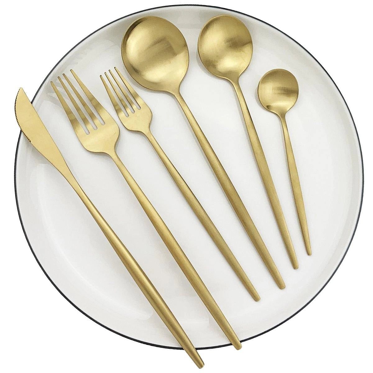 A 36-piece matte gold stainless steel cutlery set featuring modern minimalist flatware design, including forks, knives, and spoons, elegantly arranged alongside a white plate on a dining table with linen napkins.