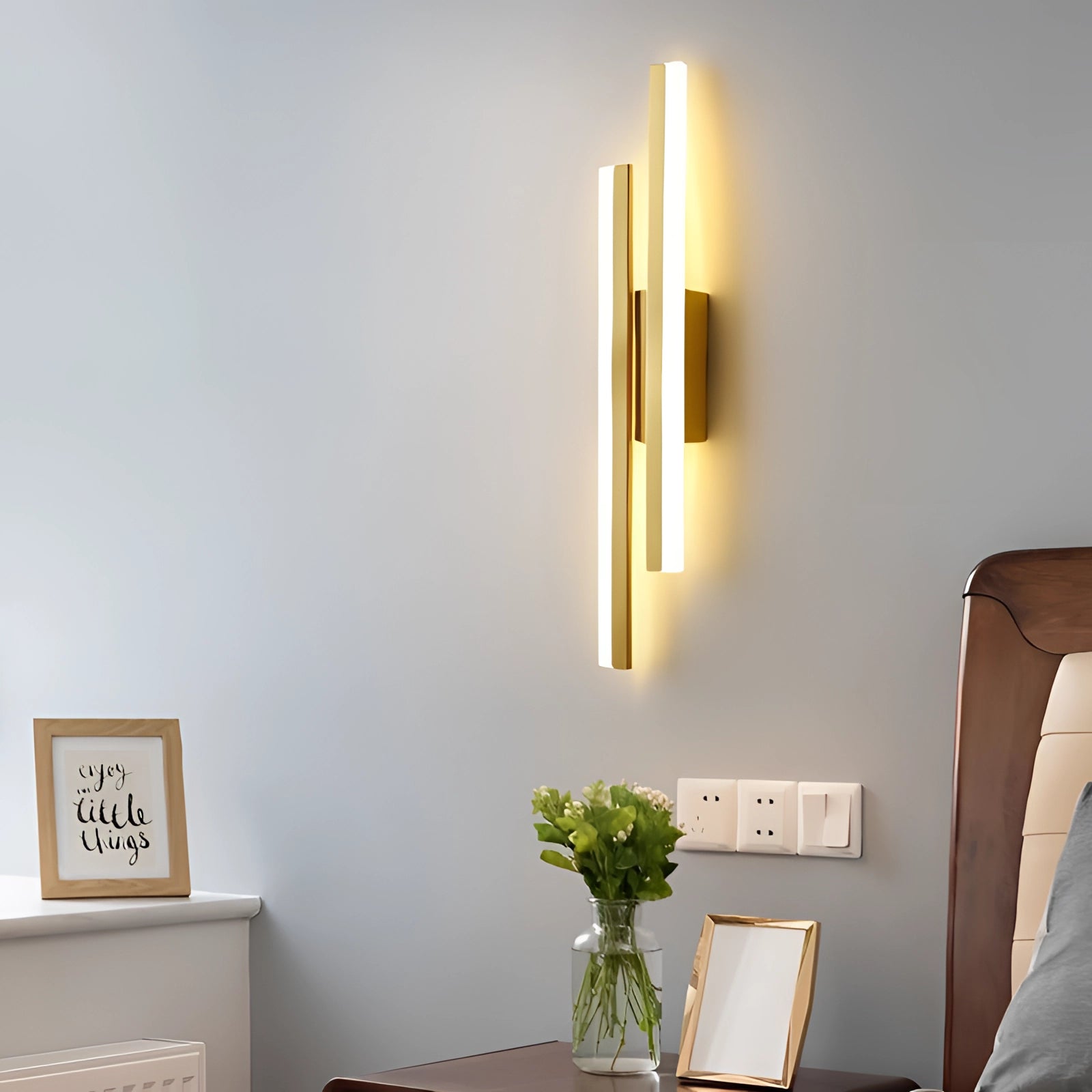 Minimalist black and white vertical line art displayed above a piece of modern furniture, with a gold frame, and a houseplant in a sleek vase nearby, creating a contemporary and comfortable decor setting.