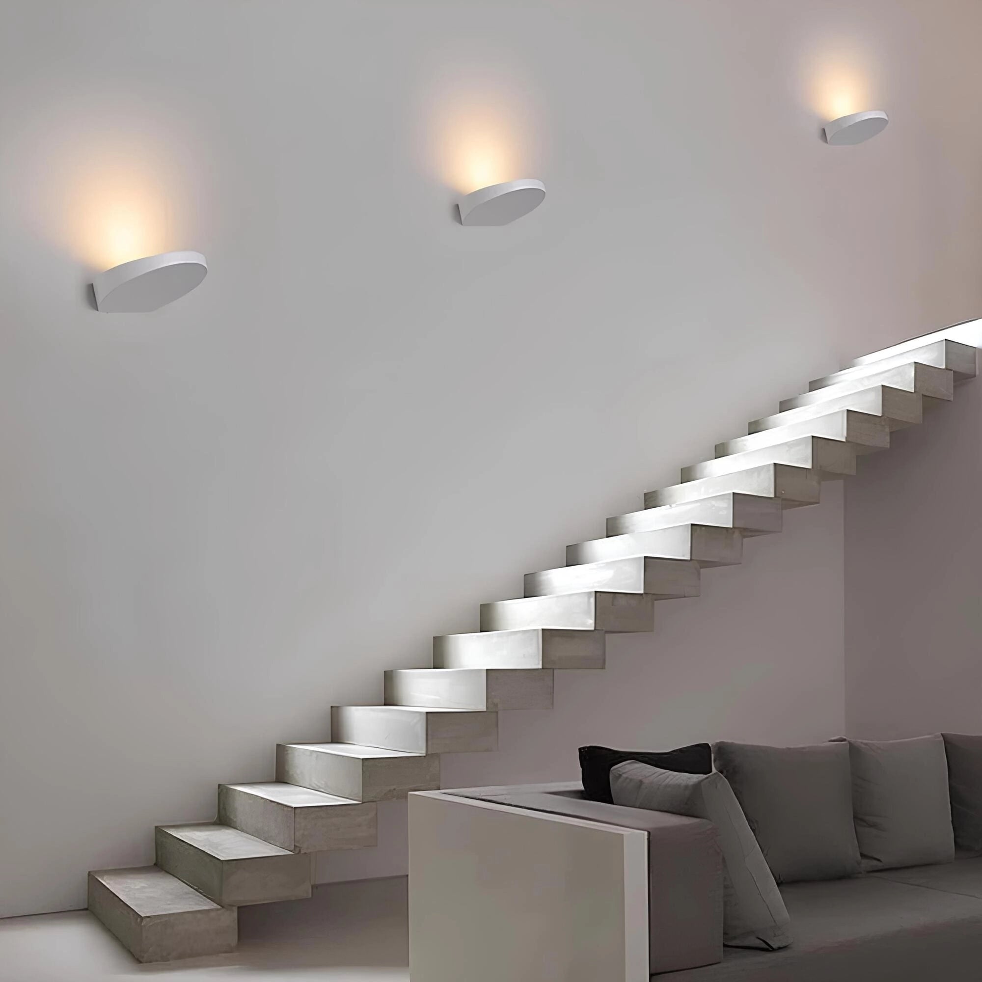 Gray sofa with wooden legs placed in a minimalist living room, accompanied by a sleek coffee table, textured rug, and a modern lamp, with a light gray wall and wooden flooring enhancing the space.