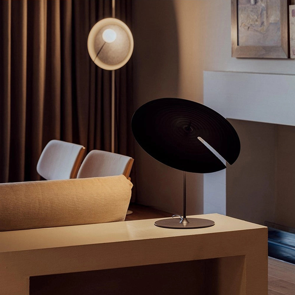 Minimalist matte black table lamp with adjustable lighting, featuring a warm white light, placed on a wooden table in a cozy interior setting.