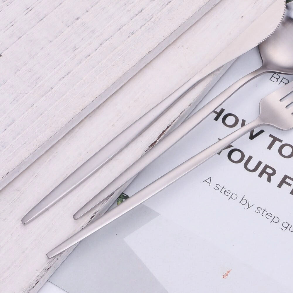 A set of minimalist stainless steel cutlery featuring an elegant and modern design with smooth, reflective surfaces, showcasing a set of forks, knives, and spoons arranged neatly.