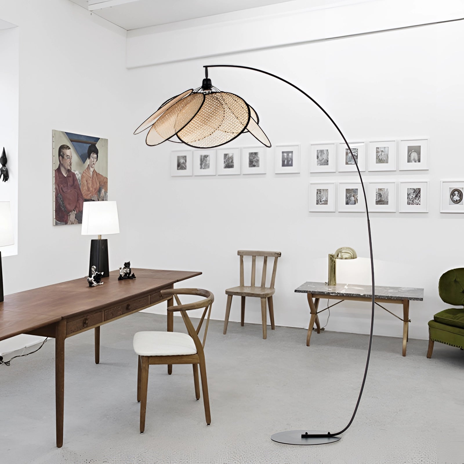 Modern adjustable arched floor lamp in a minimalist design, positioned next to a wooden table and chair in a well-lit interior space with a picture frame on the wall.