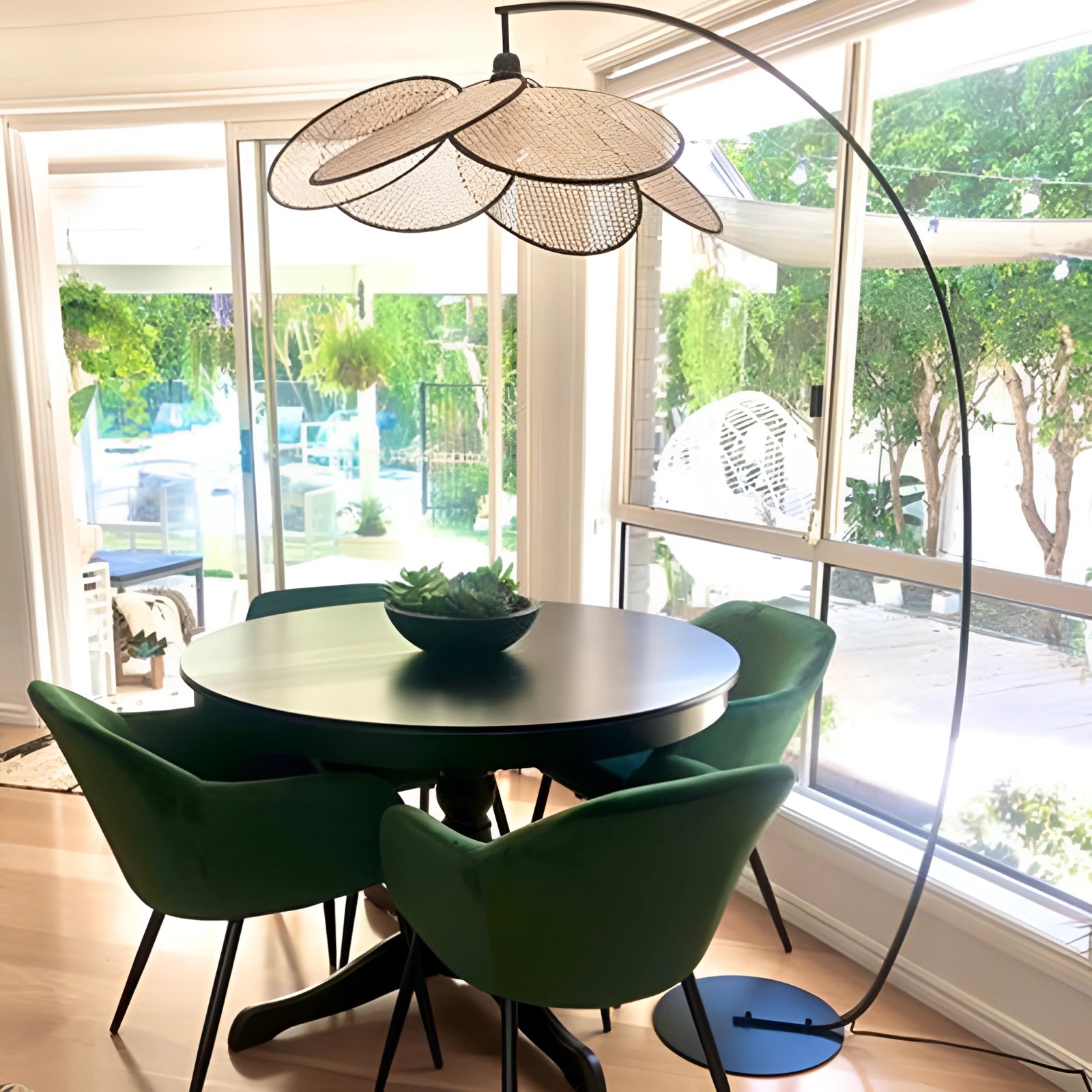 Modern adjustable arched floor lamp with minimalist design, positioned next to a table and chair, featuring a sleek shade, indoor plant, and stylish interior setting.