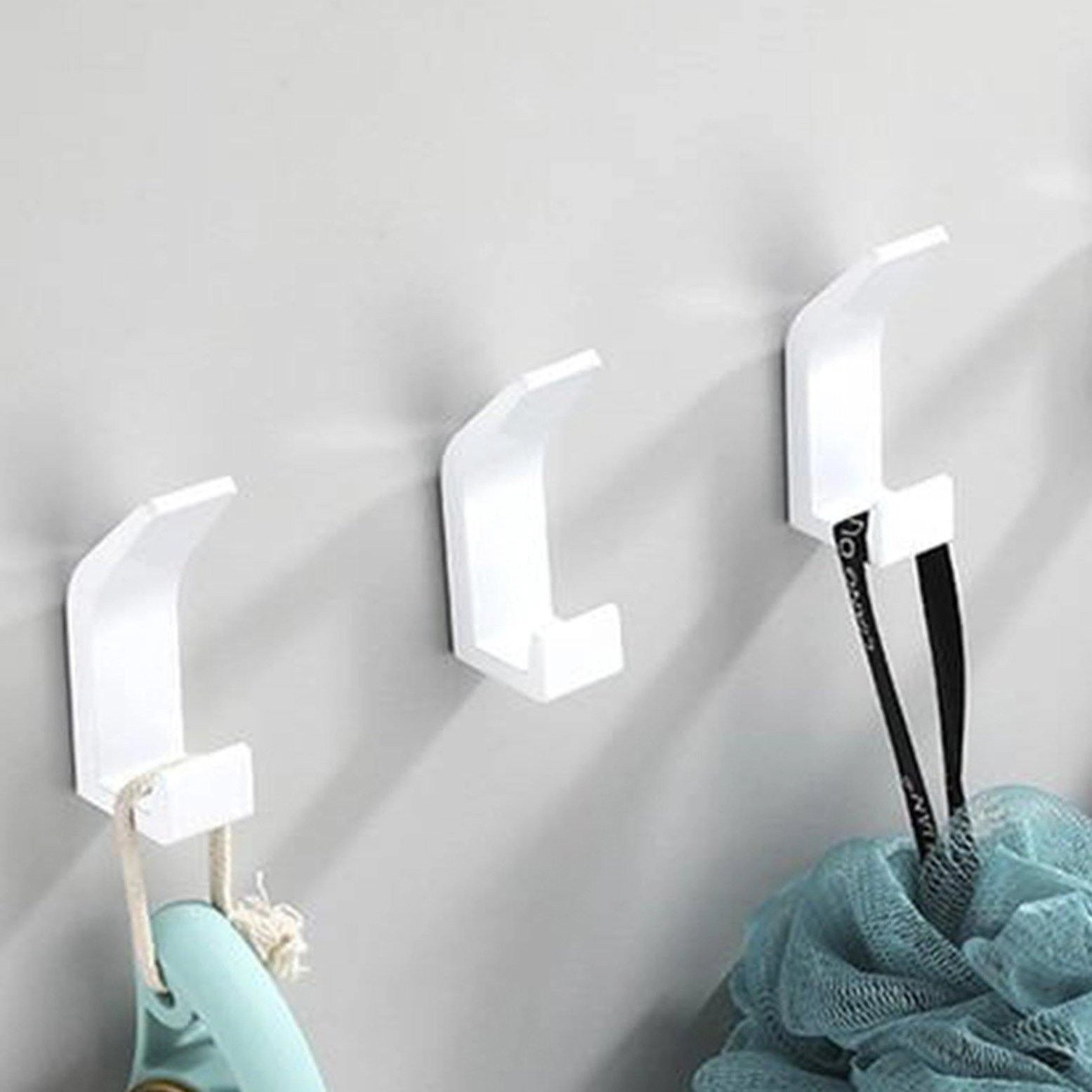 Minimalistic and stylish white modern black metal wall hooks mounted on a white wall in a well-designed interior setting featuring a ceiling lamp, wooden flooring, and contemporary decor elements.