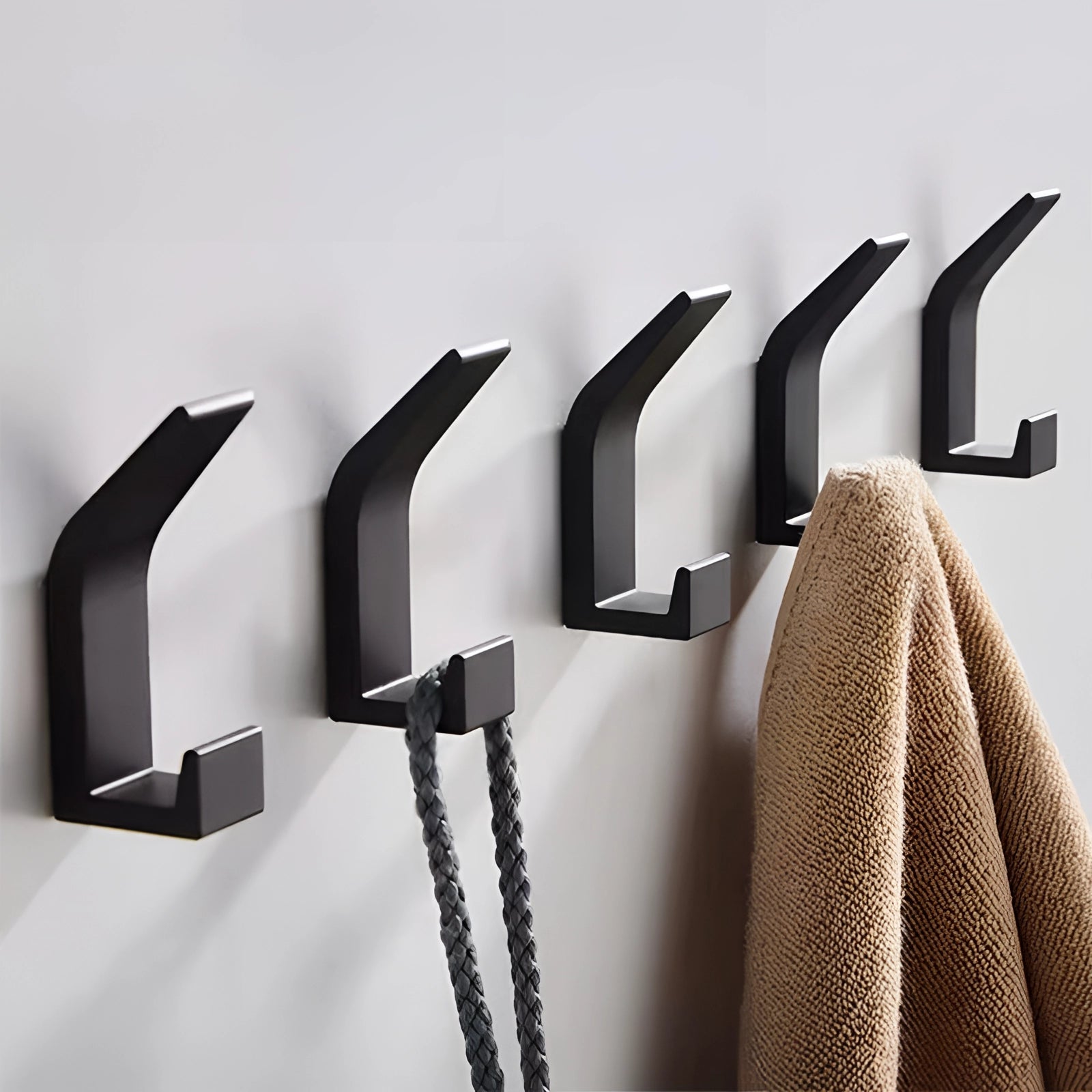A set of five modern black metal wall hooks with a minimalist and stylish design, mounted on a wooden surface.