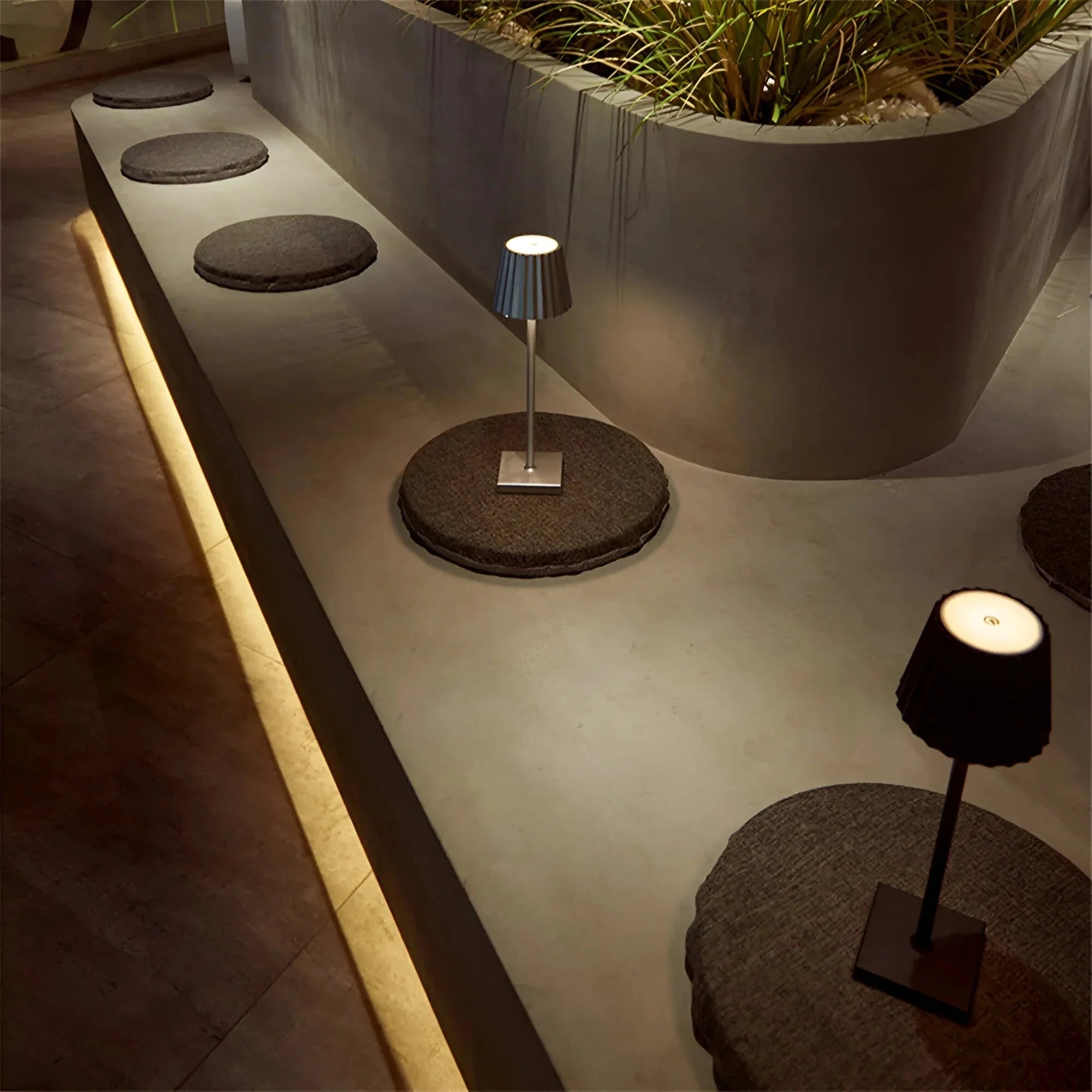 A modern black minimalist table lamp with a slim profile, elegantly illuminating a room with wooden flooring, complemented by a plant in a flowerpot, showcasing a stylish interior design.