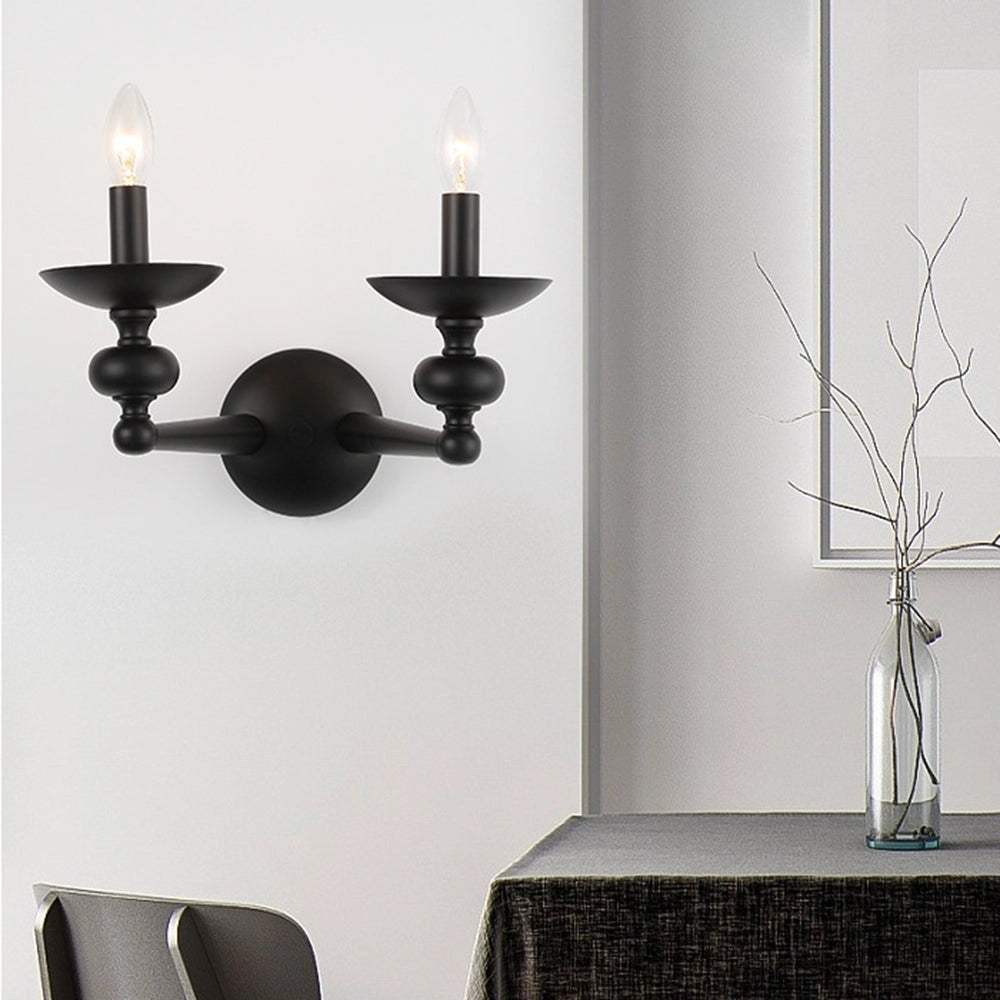 Modern black two-head chandelier with six candle-style lights, elegantly hanging above a dining table in a stylishly designed interior space. The room features a monochromatic color palette with white and grey elements, including a rectangular table and wall art.