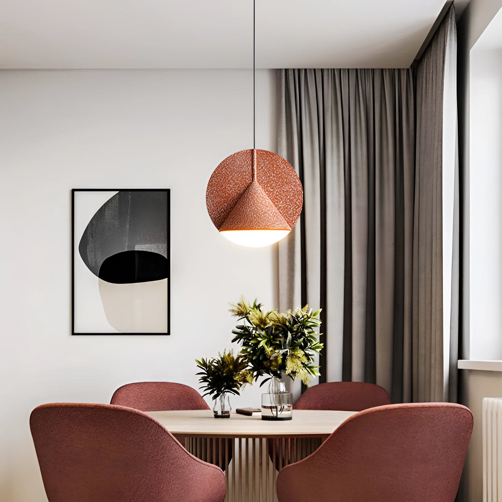 Modern colorful fabric pendant light in orange hanging above a wooden table with chairs, plants, and other interior decor elements in a contemporary setting.