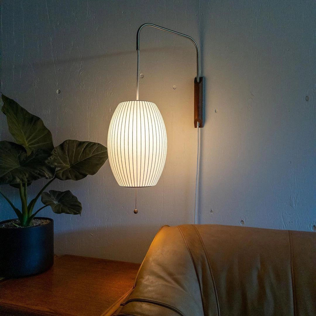 Modern floor lamp featuring minimalist design with adjustable brass and wood accents, positioned next to a houseplant and flowerpot in a stylish interior setting.