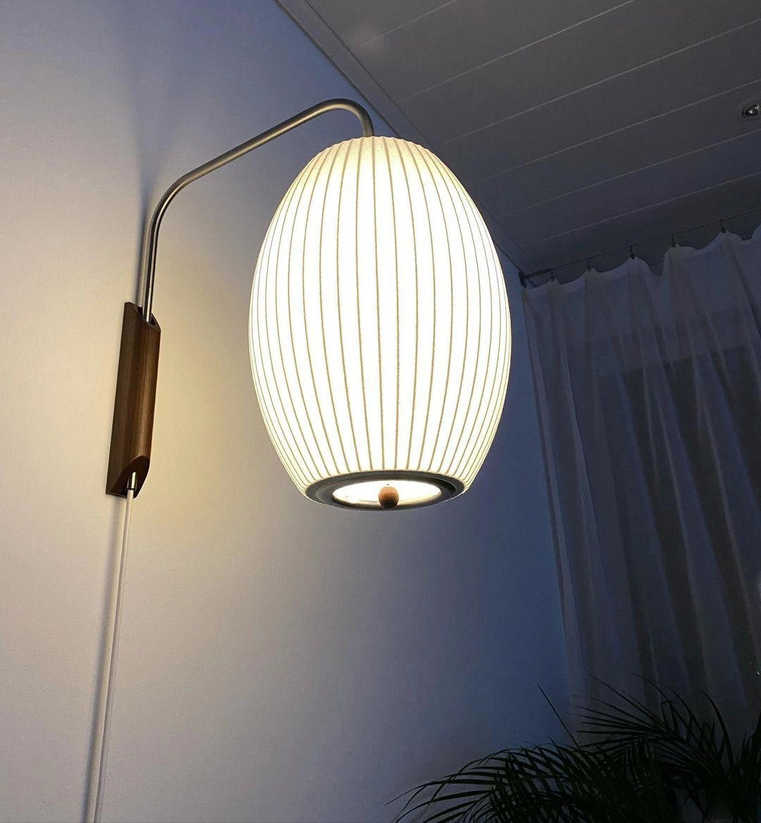 Modern floor lamp with a minimalist design featuring adjustable brass and wood accents, displaying a round shade and standing in front of a neutral backdrop.