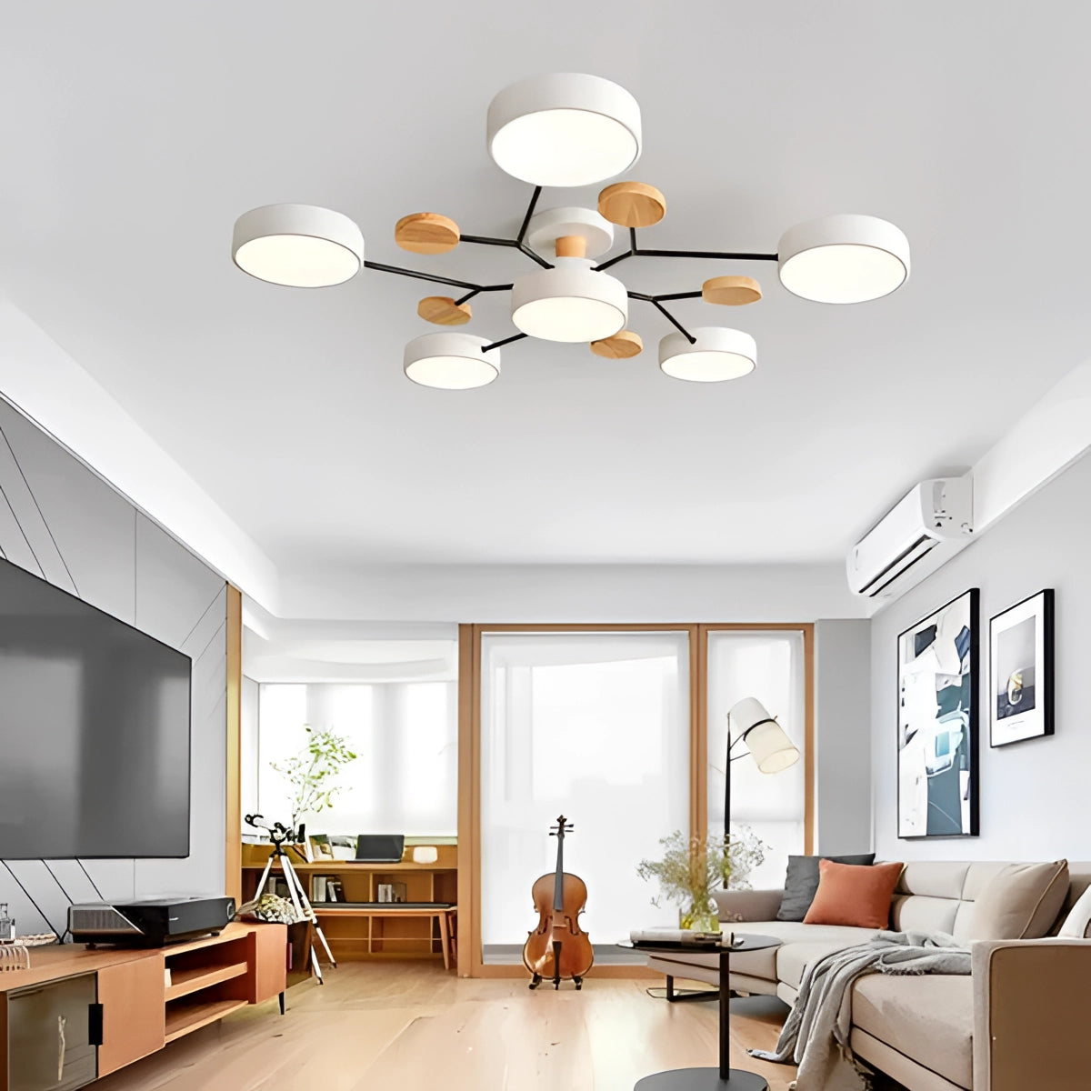 Modern geometric chandelier with matte black and wood finish, featuring multiple bulbs, hanging in a stylish interior setting with white walls. The room includes a cozy living room area with a couch, a houseplant, and a warm ambiance created by orange and yellow lighting accents.