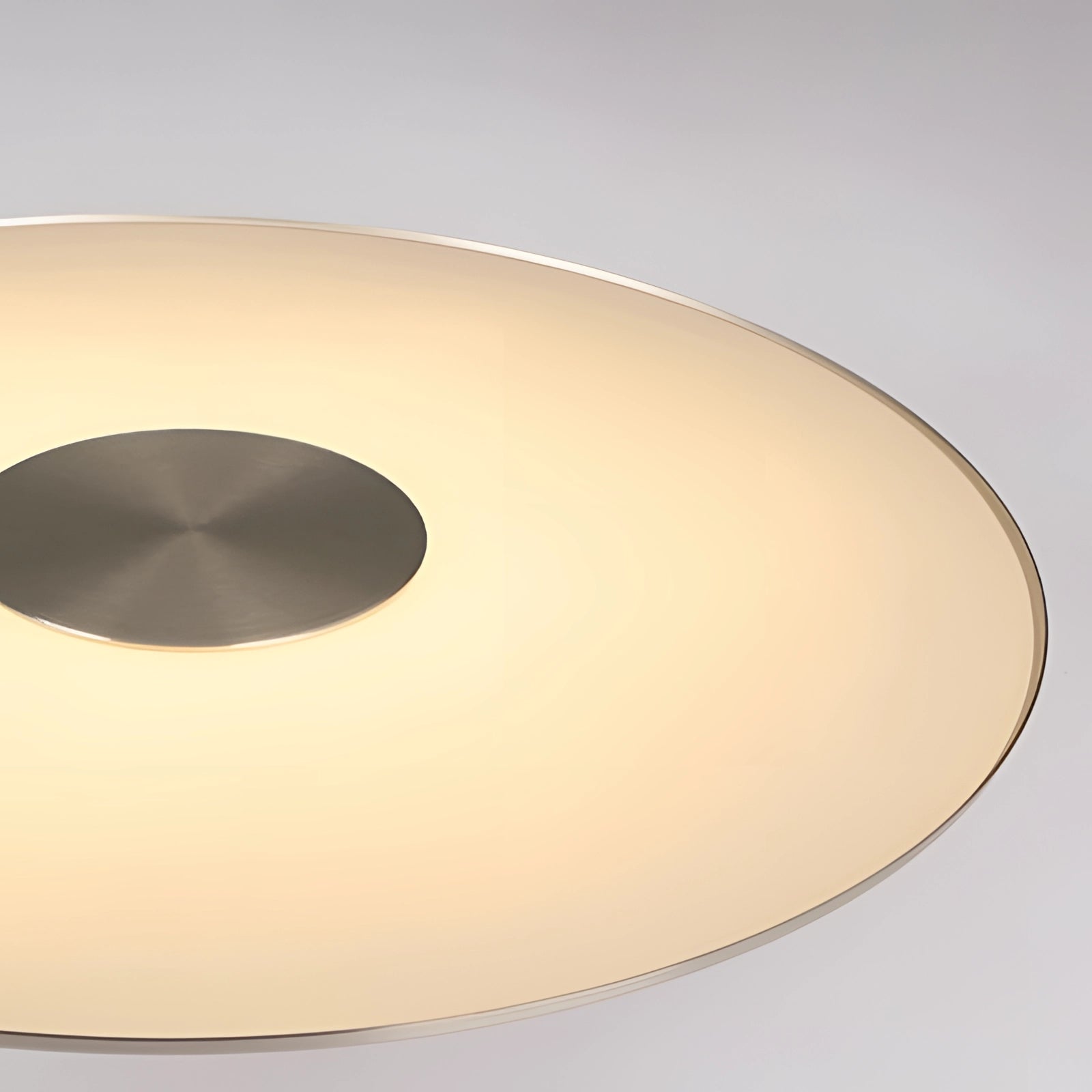 Modern gold-brushed pendant light hanging from a ceiling, featuring a sleek metal finish and circular design, illuminating a dining or kitchen area with a warm glow. The background includes hints of a wooden table and minimalistic decor elements.