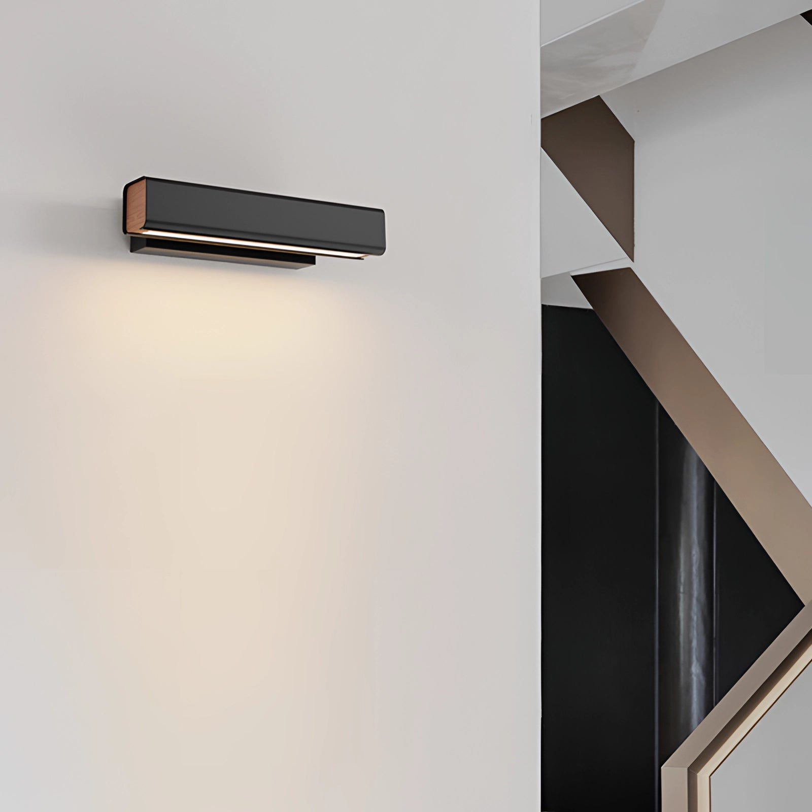 Modern LED wall sconce in black with gold accents, featuring a sleek rectangular design and an adjustable arm, mounted on a grey wall. The lamp emits a cold white light, suitable for contemporary interiors.