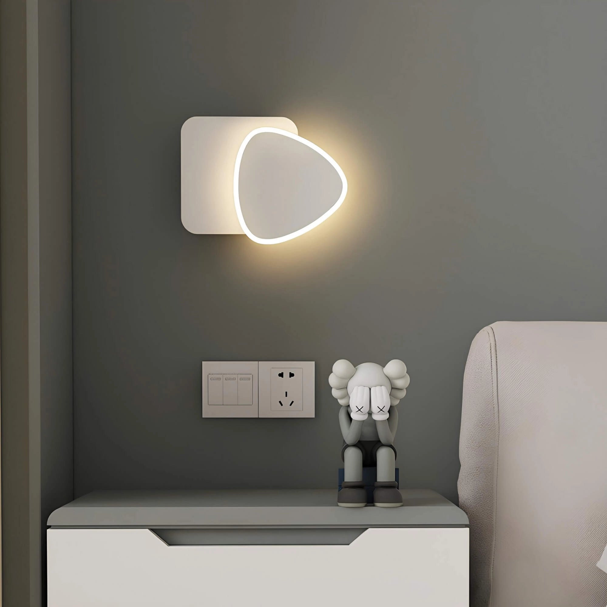Modern LED wall sconce with a geometric minimalist design, featuring a rectangular grey shape mounted on a wooden interior wall, adding a contemporary touch to the room's decor.