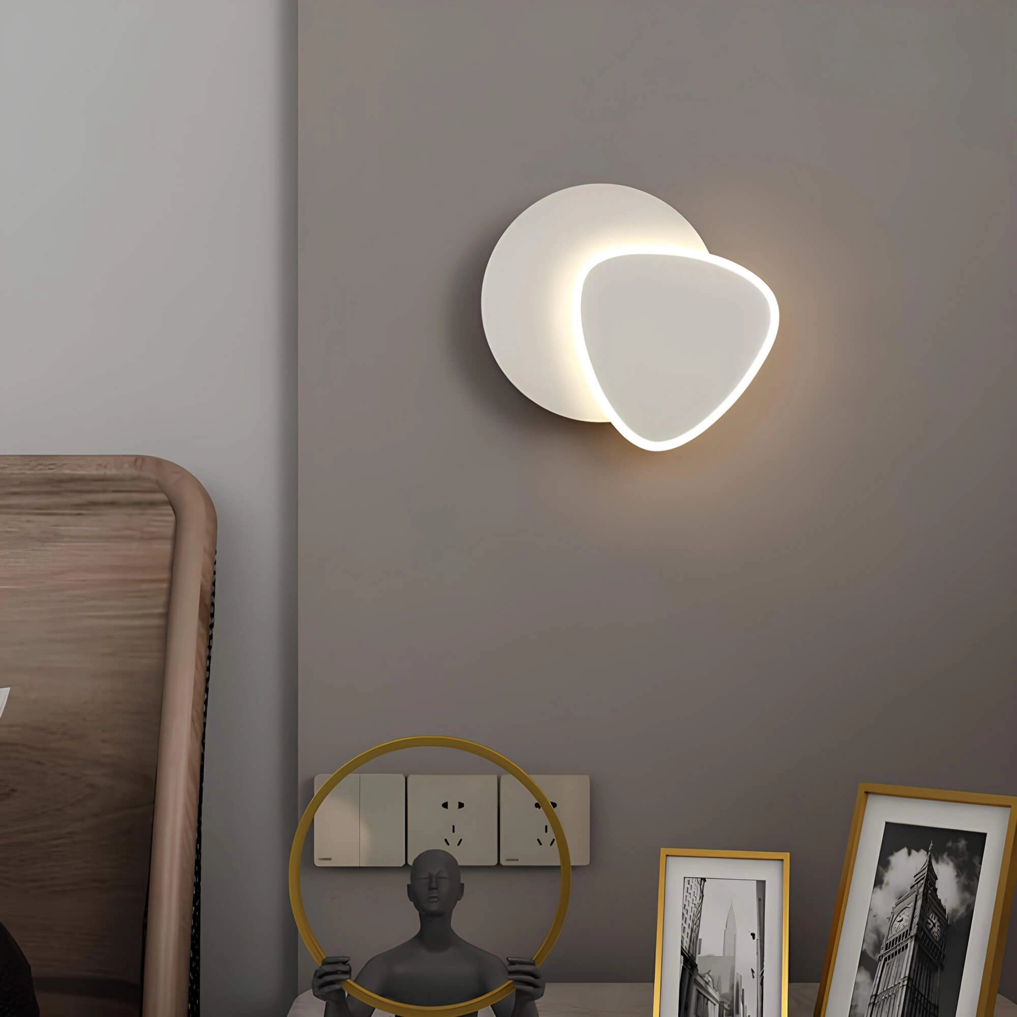 Modern LED wall sconce with a geometric minimalist design mounted on an indoor wall, illuminating a contemporary living space featuring wooden elements and a picture frame beside a window.