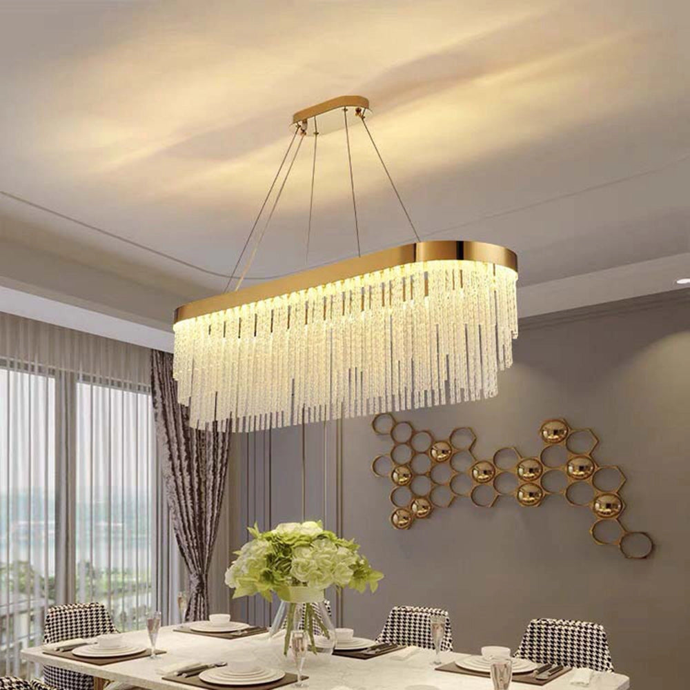 Modern luxury circular crystal LED chandelier with brass finish, elegantly suspended above a contemporary table adorned with decorative tableware and surrounded by stylish interior elements, including greenery and wooden accents.