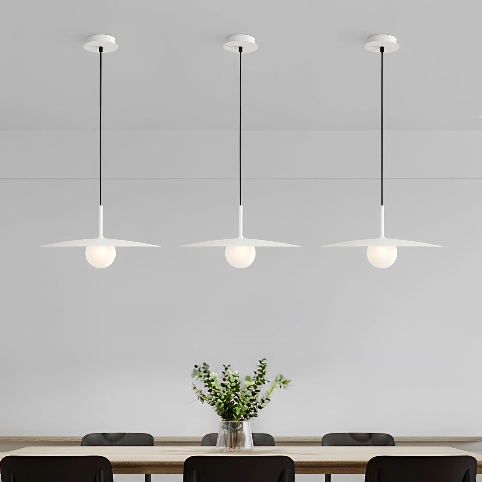 Modern minimalist LED pendant light with a Scandinavian dual-tone design hanging above a white table, surrounded by a houseplant on the side, a chair, and decorative art elements in a contemporary setting.