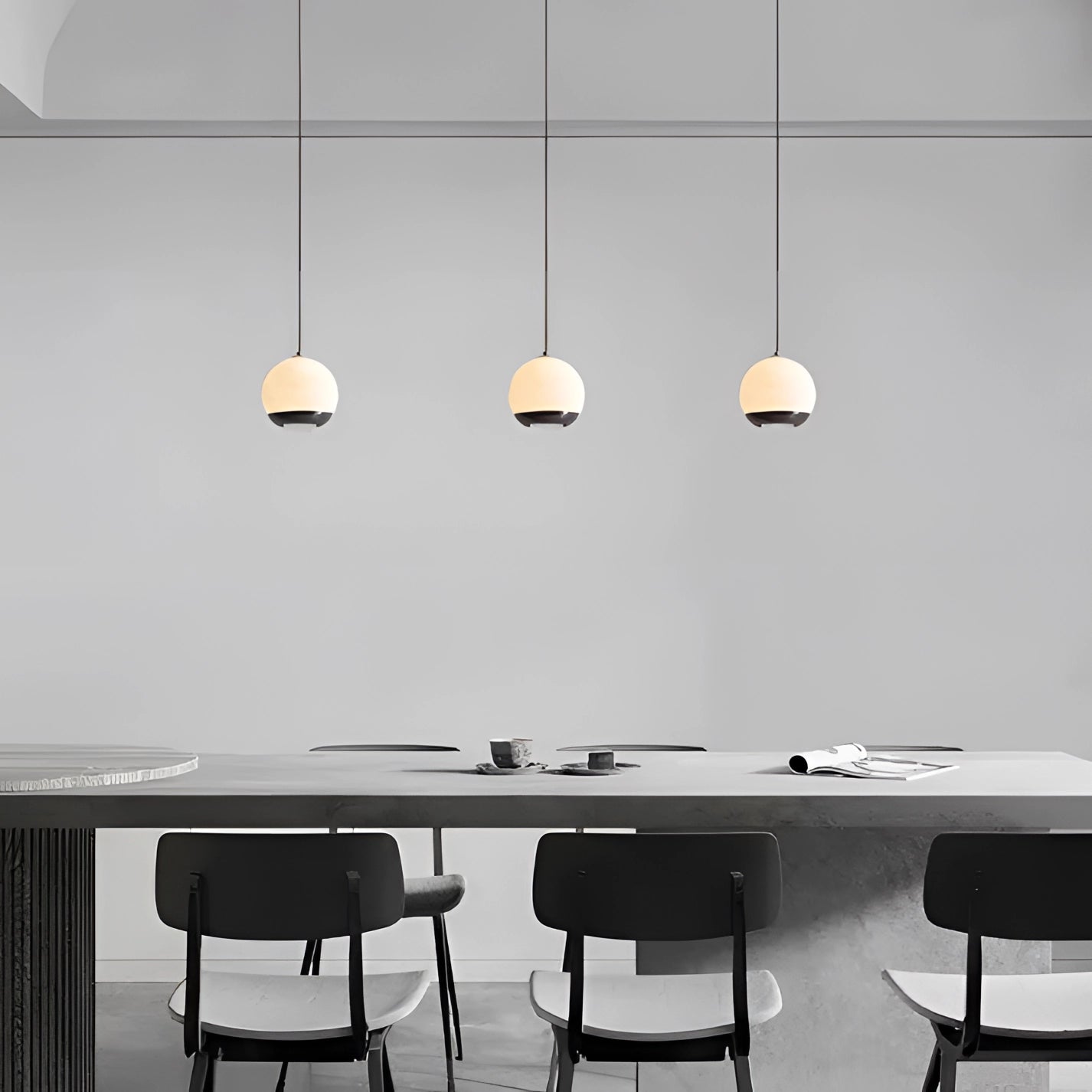 Modern minimalist white spherical pendant light hanging above a wooden table and chair set in a stylish bedroom with light flooring and contemporary interior design.