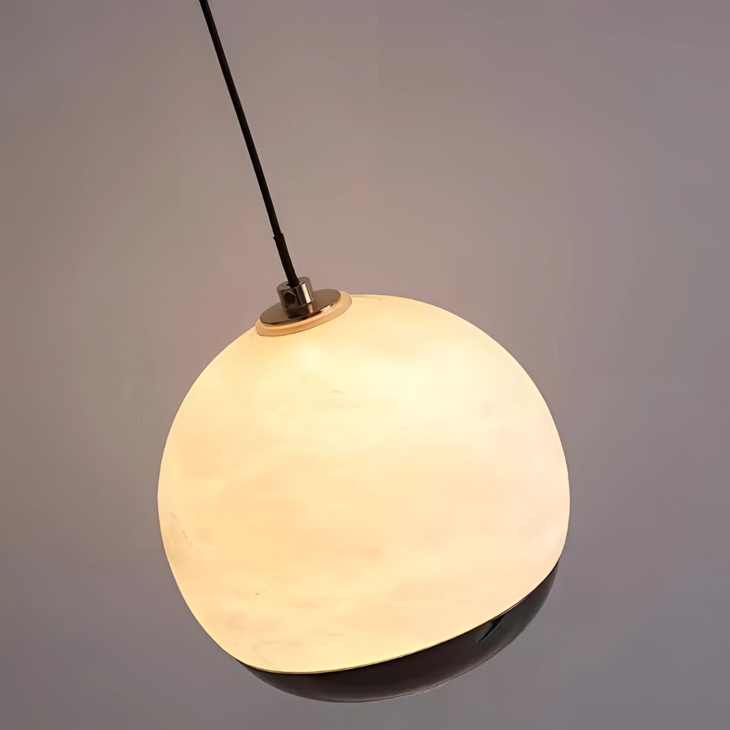 Modern minimalist white spherical pendant light hanging in a bedroom, illuminating a wooden table with decorative ornaments and artistic elements.