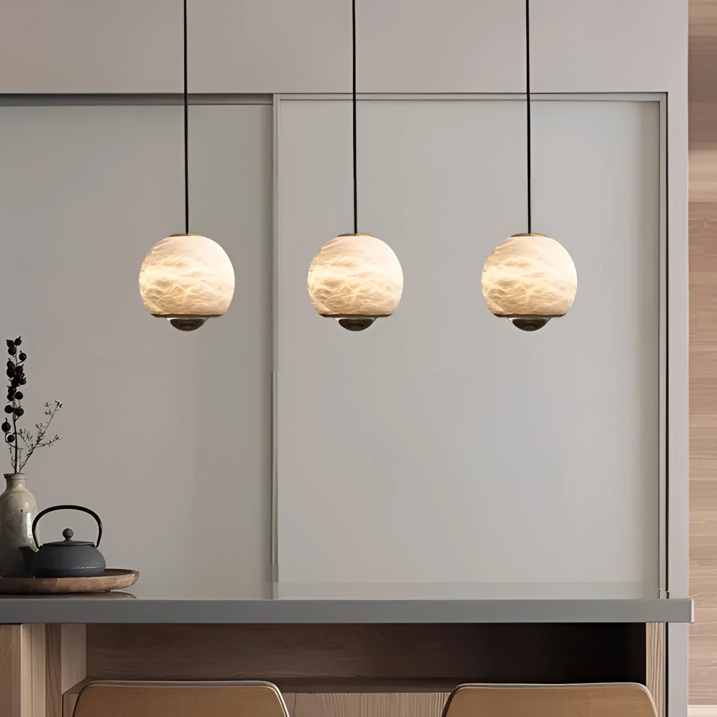Modern minimalist white spherical pendant light hanging from the ceiling, with a background featuring wooden shelving, plants, wall art, and light-colored flooring.
