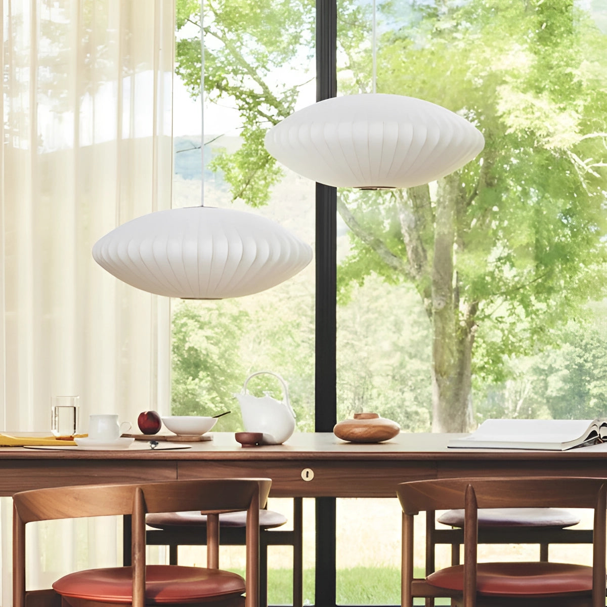 Modern oval pendant lights hanging over a contemporary dining room table with wooden furniture, surrounded by indoor plants, large windows, and stylish interior design elements.