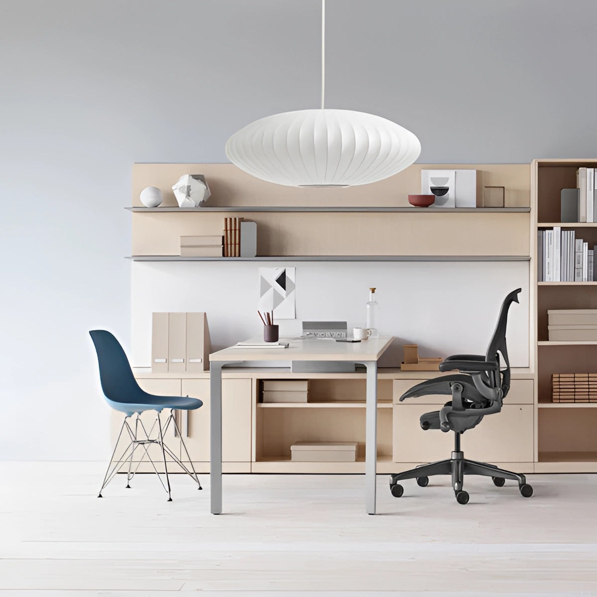 Modern oval pendant lights hanging above a contemporary dining room setting featuring a wooden table and chairs, with shelving visible in the background.