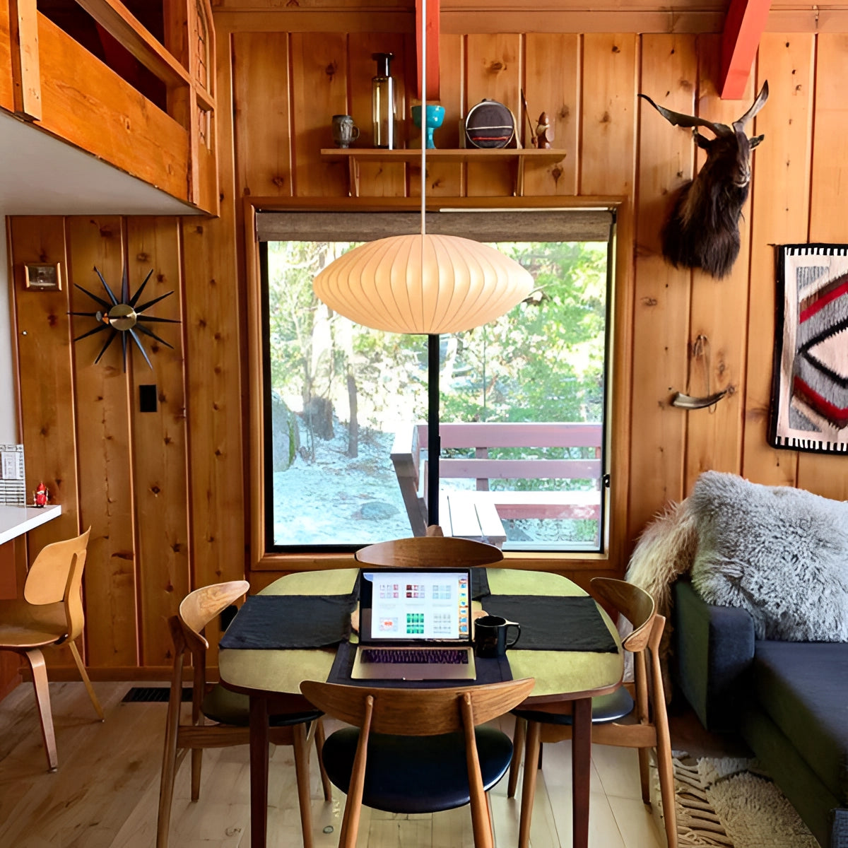 Modern oval pendant lights hanging above a contemporary dining room table set with wooden chairs, showcasing interior design elements with natural lighting from nearby windows.