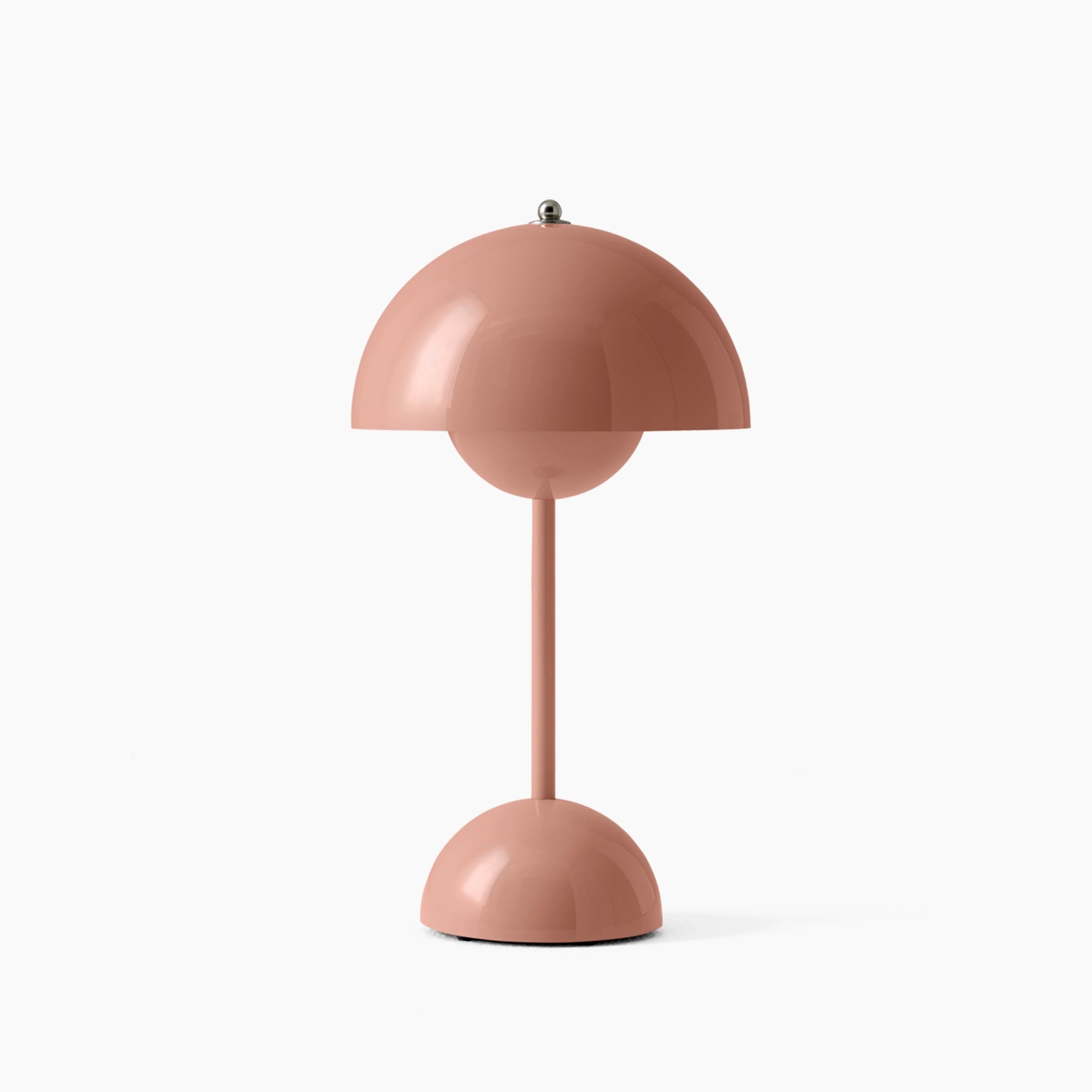 Modern peach table lamp with an adjustable minimalist spherical design, featuring a soft pink hue, placed beside a small potted plant.