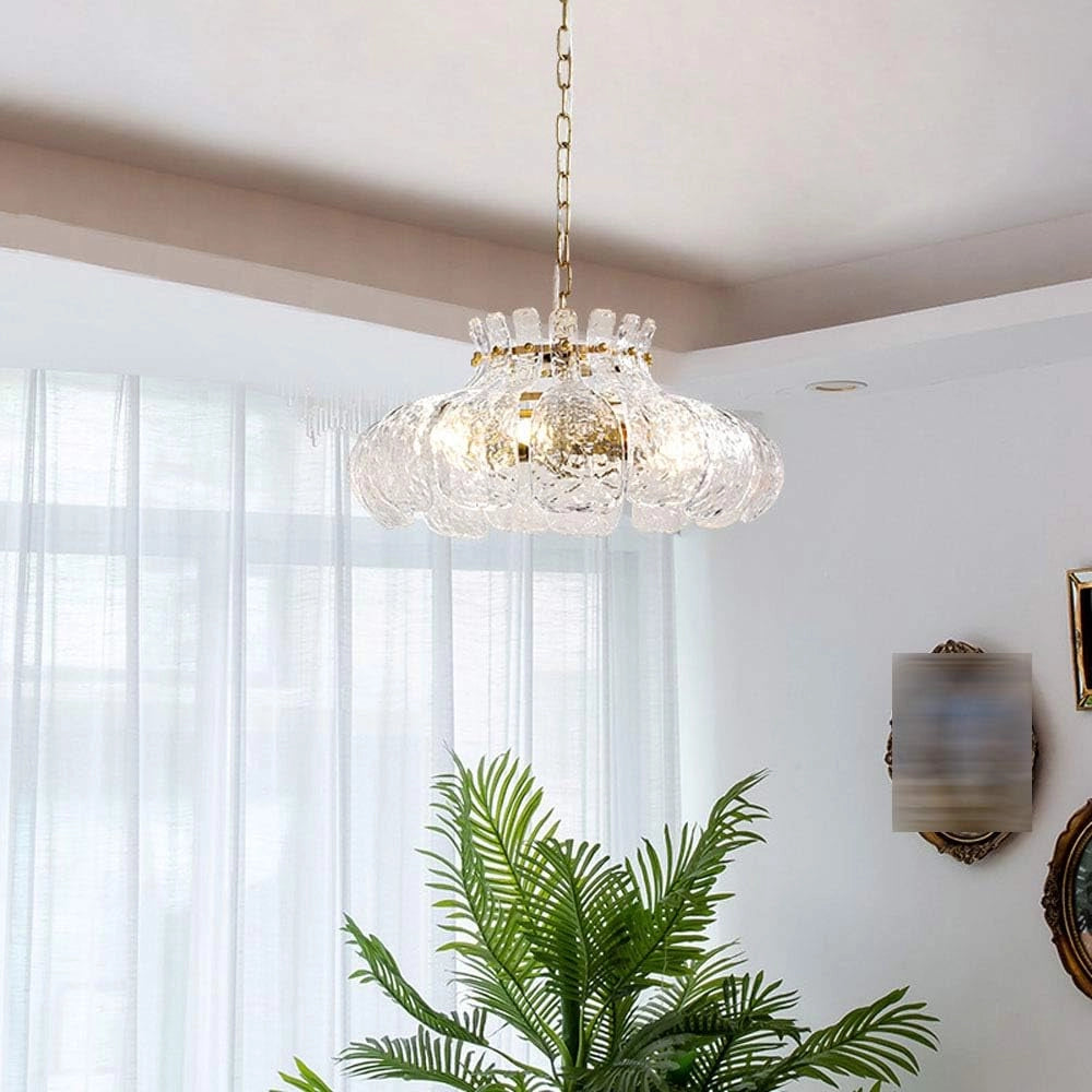 Modern pear-shaped glass chandelier with gold chain, hanging from the ceiling in a stylish interior setting, surrounded by houseplants and wooden elements, providing luxurious lighting to the space.
