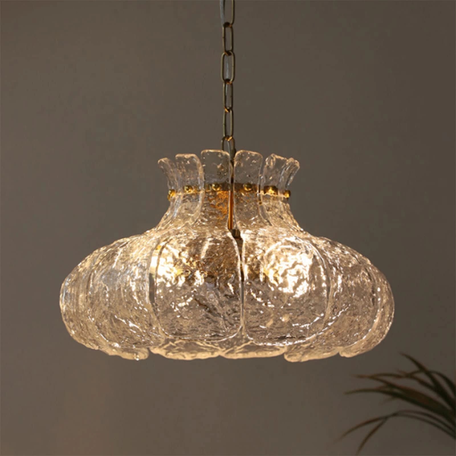 Modern pear-shaped glass chandelier with a luxurious gold chain, featuring multiple light bulbs and a circular design, hanging from a ceiling.