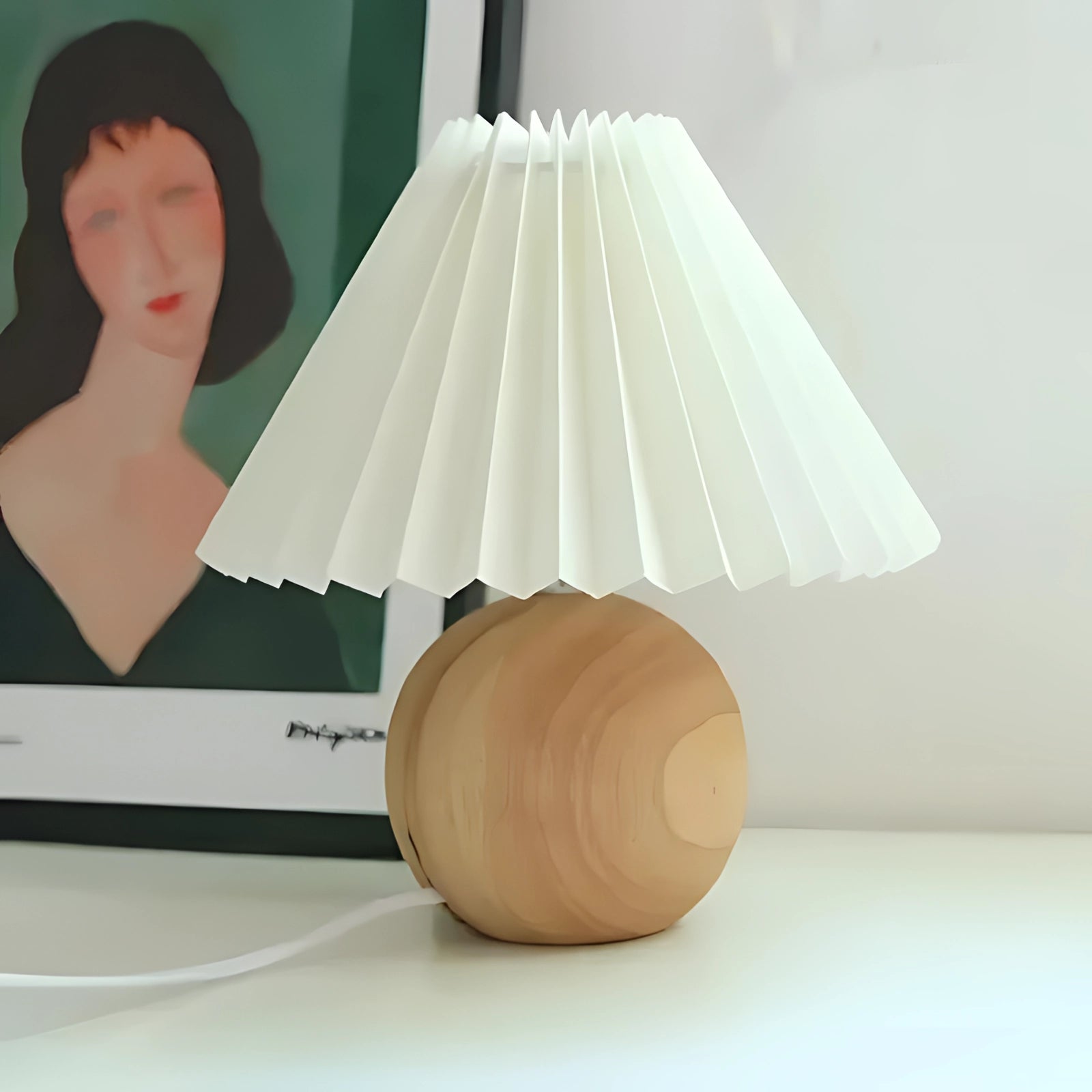 Modern pink ceramic lamp with pleated shade featuring a Scandinavian design, shown with a white wood base, placed in a room setting.