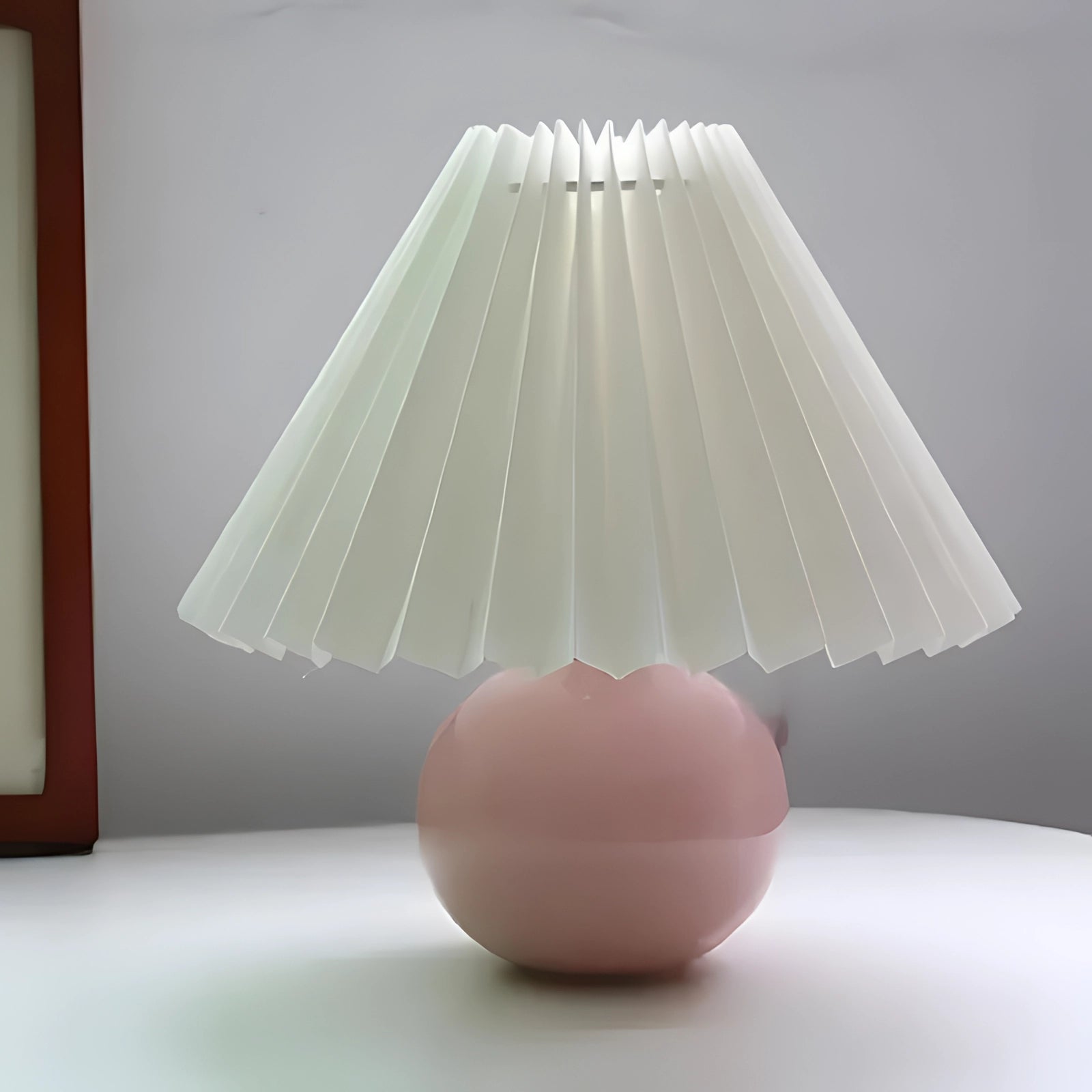 Modern pink ceramic table lamp with a pleated shade in a Scandinavian design, featuring white and pink colors, standing on a wooden base.