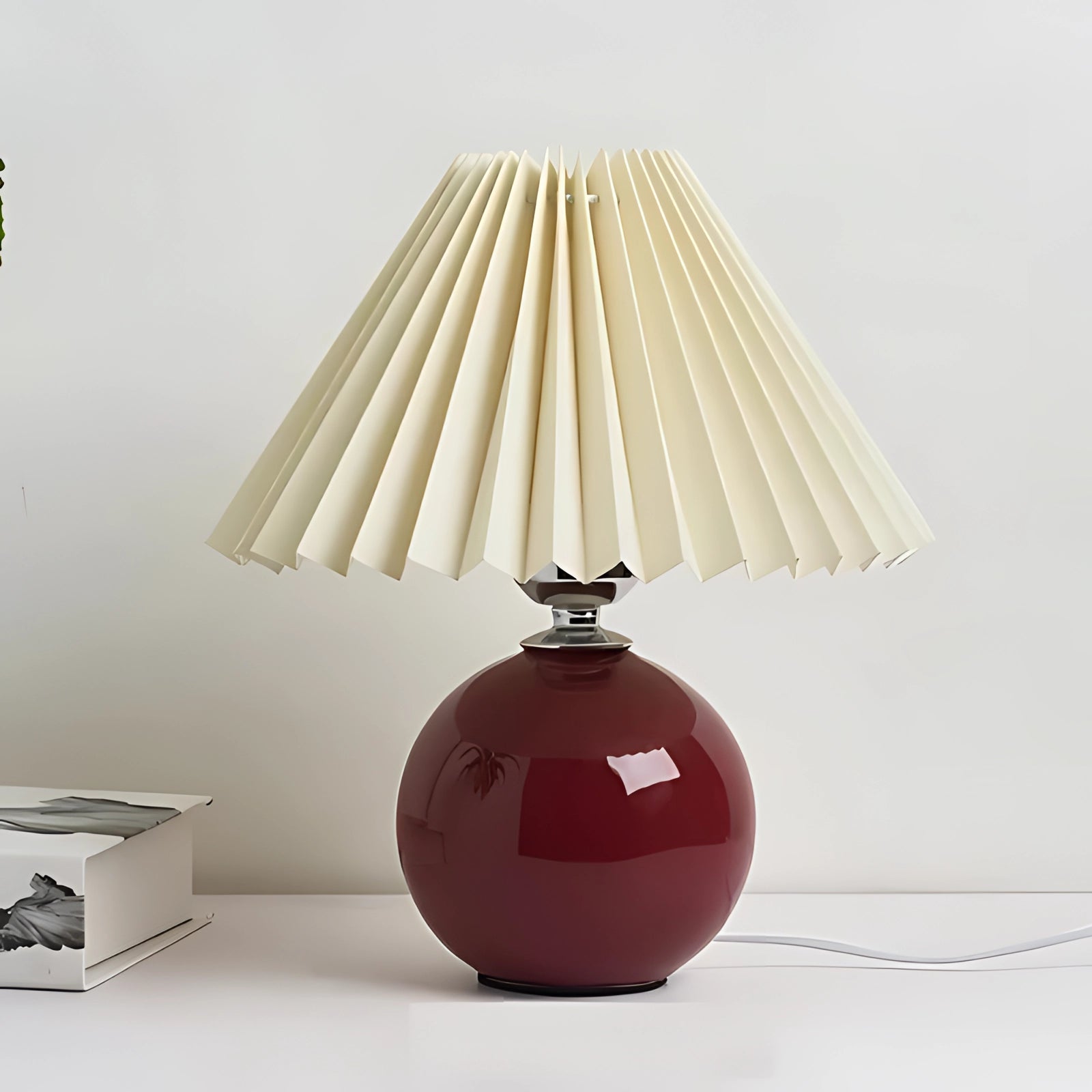 Modern pink ceramic table lamp with a pleated cream red shade, featuring Scandinavian design elements and a natural wood base, set in a contemporary interior space.
