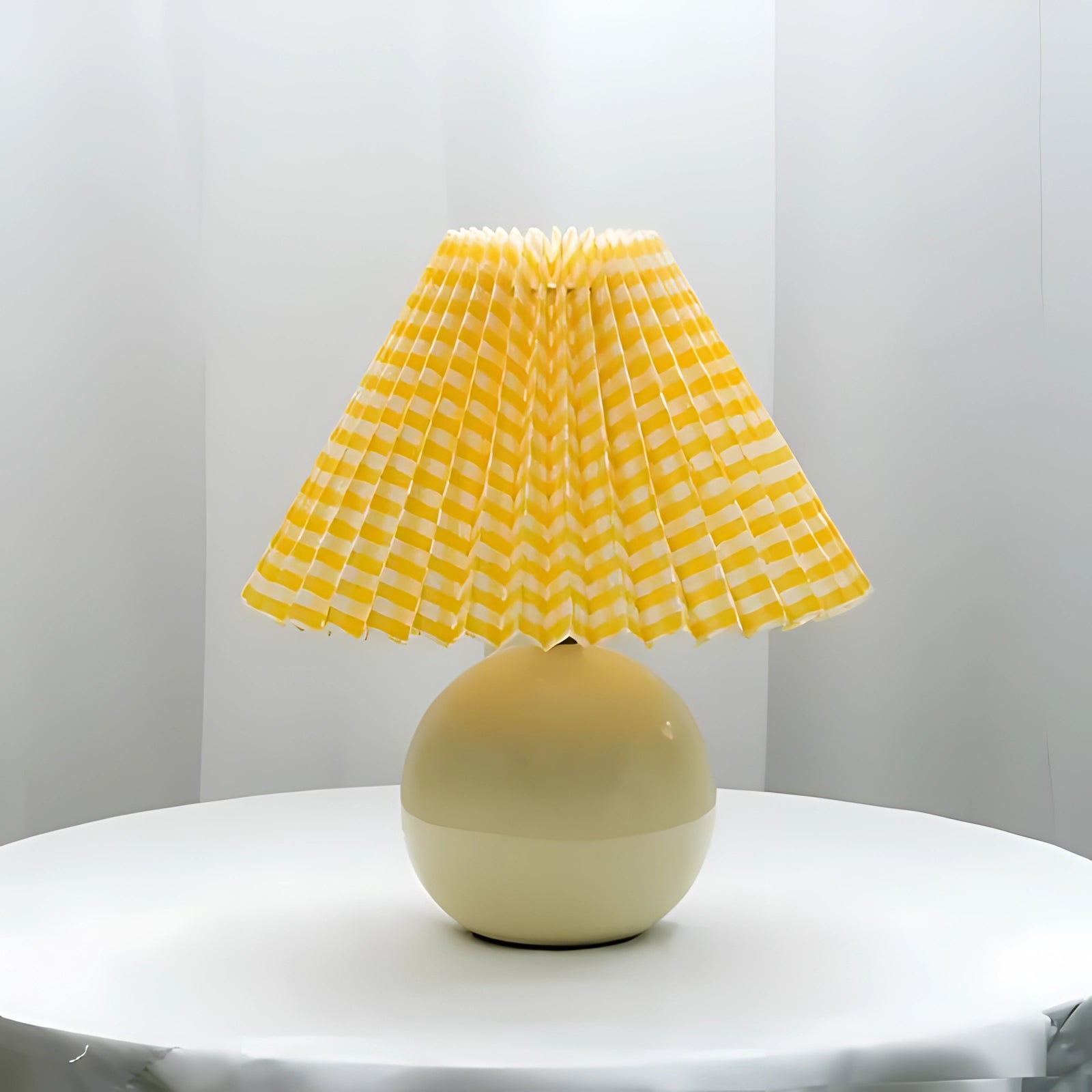 Modern pink ceramic lamp with a pleated shade in a Scandinavian design, featuring a yellow and white color variant, placed on a wooden table in an interior setting.
