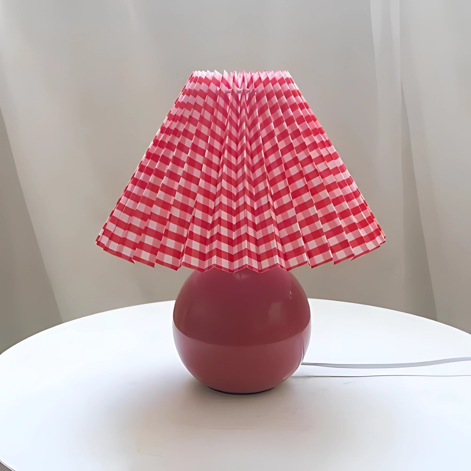 Modern pink ceramic lamp with a pleated shade in a Scandinavian design, featuring a sleek, triangular base and a soft magenta hue, placed on a wooden table.