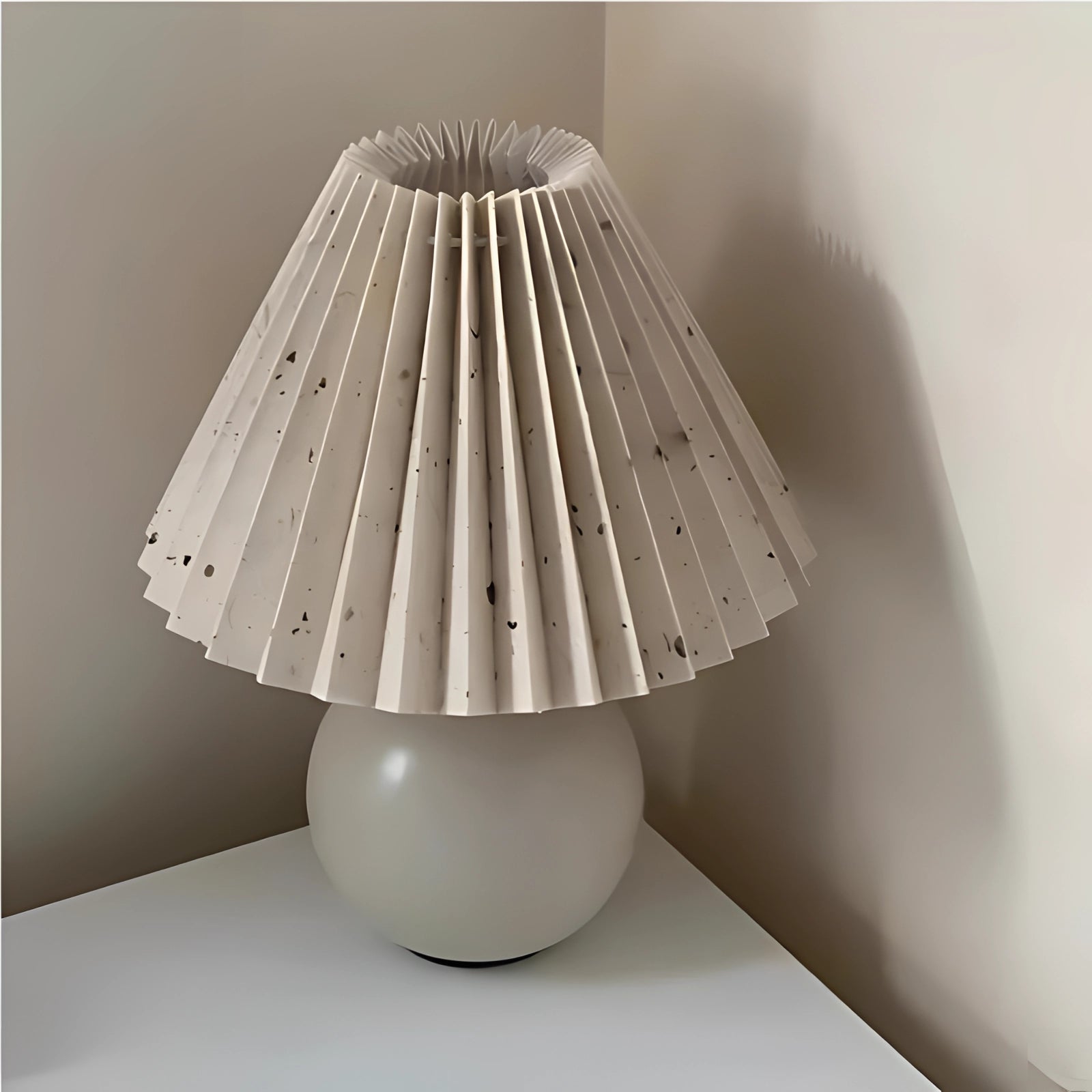 Modern pink ceramic lamp with a pleated shade, featuring a sleek Scandinavian design, displayed on a wooden table. The lamp has a white marble base, complemented by ambient tints and shades in the background.