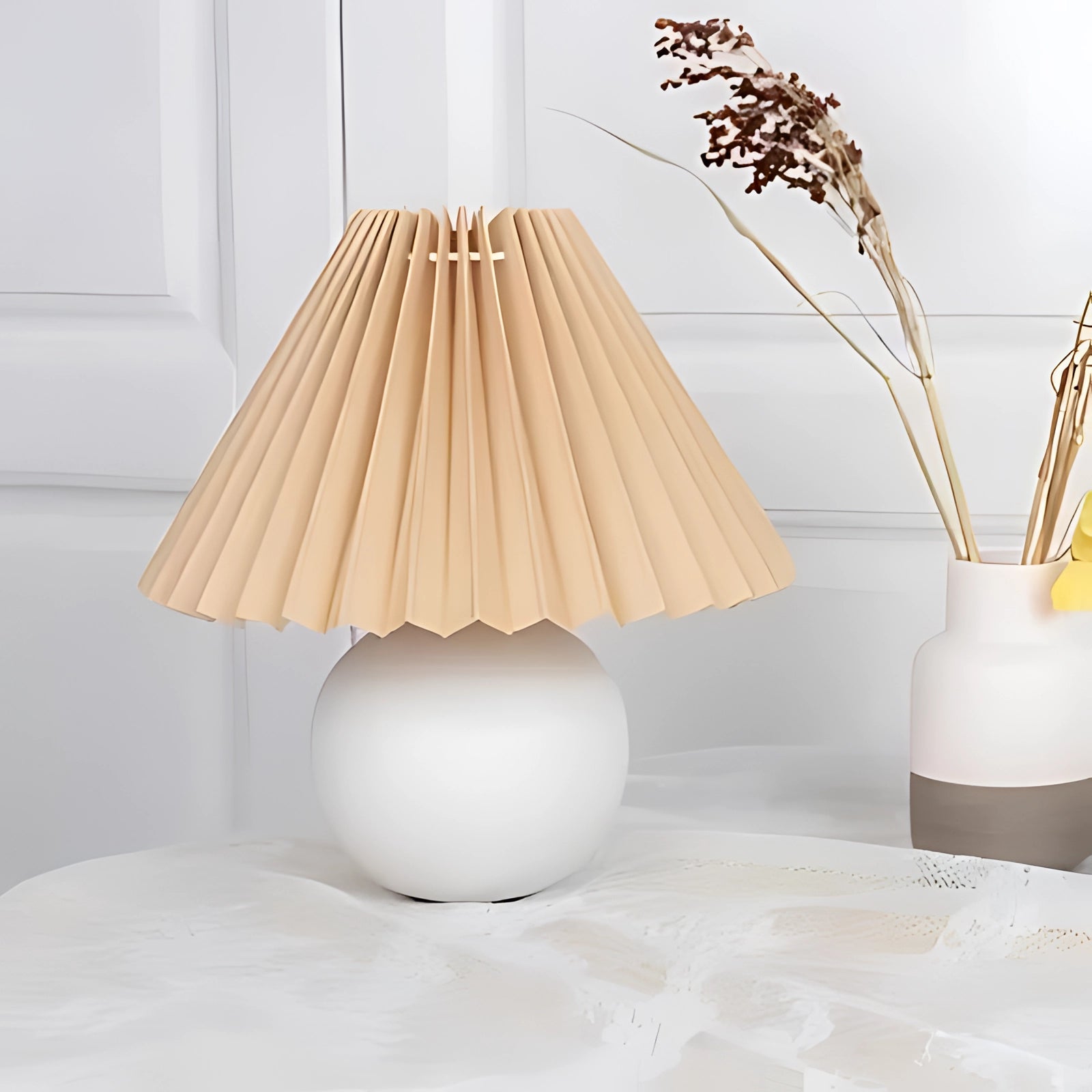 Modern pink ceramic lamp with a pleated shade placed on a wooden table in a Scandinavian-style interior, featuring beige and brown tones, complemented by natural light streaming through a window.