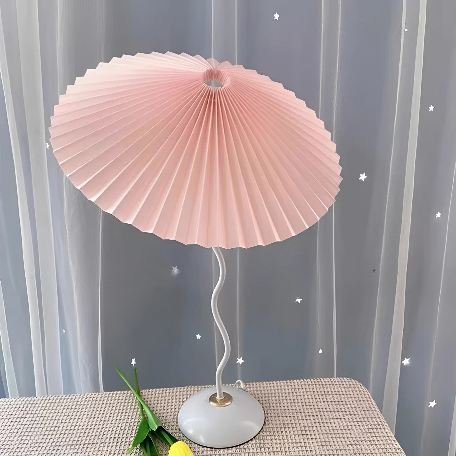 Modern pink table lamp with a pleated accordion design, featuring a stylish origami-inspired pattern. The lamp is made of textile material and includes a wooden base, adding a touch of contemporary art and interior design flair to any room setting. The vibrant magenta hue enhances the aesthetic appeal, making it an eye-catching addition to the decor.