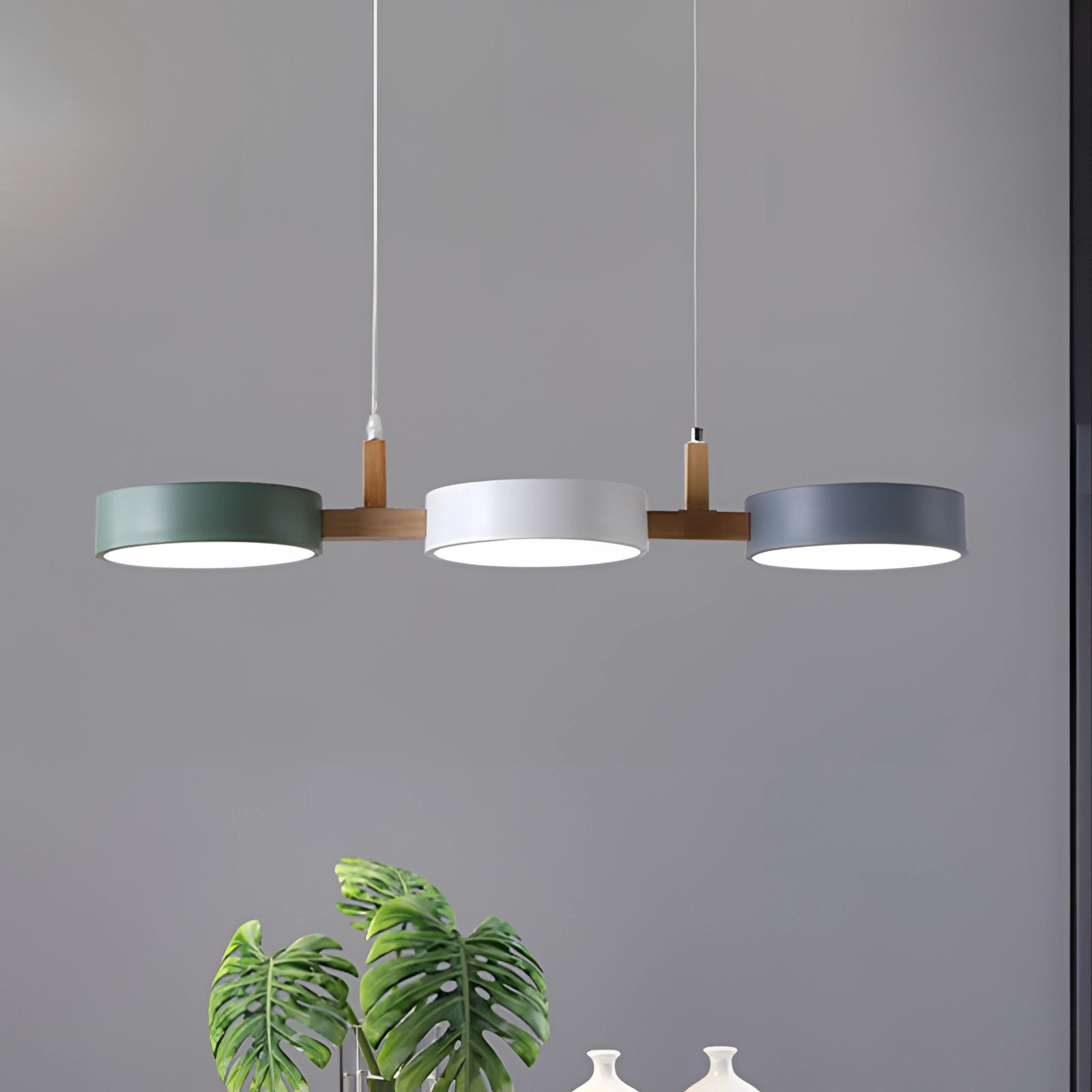 Modern Scandinavian adjustable triple pendant lights with a sleek rectangular design, featuring wooden and composite material elements, illuminating a dining room setting with a houseplant in view.