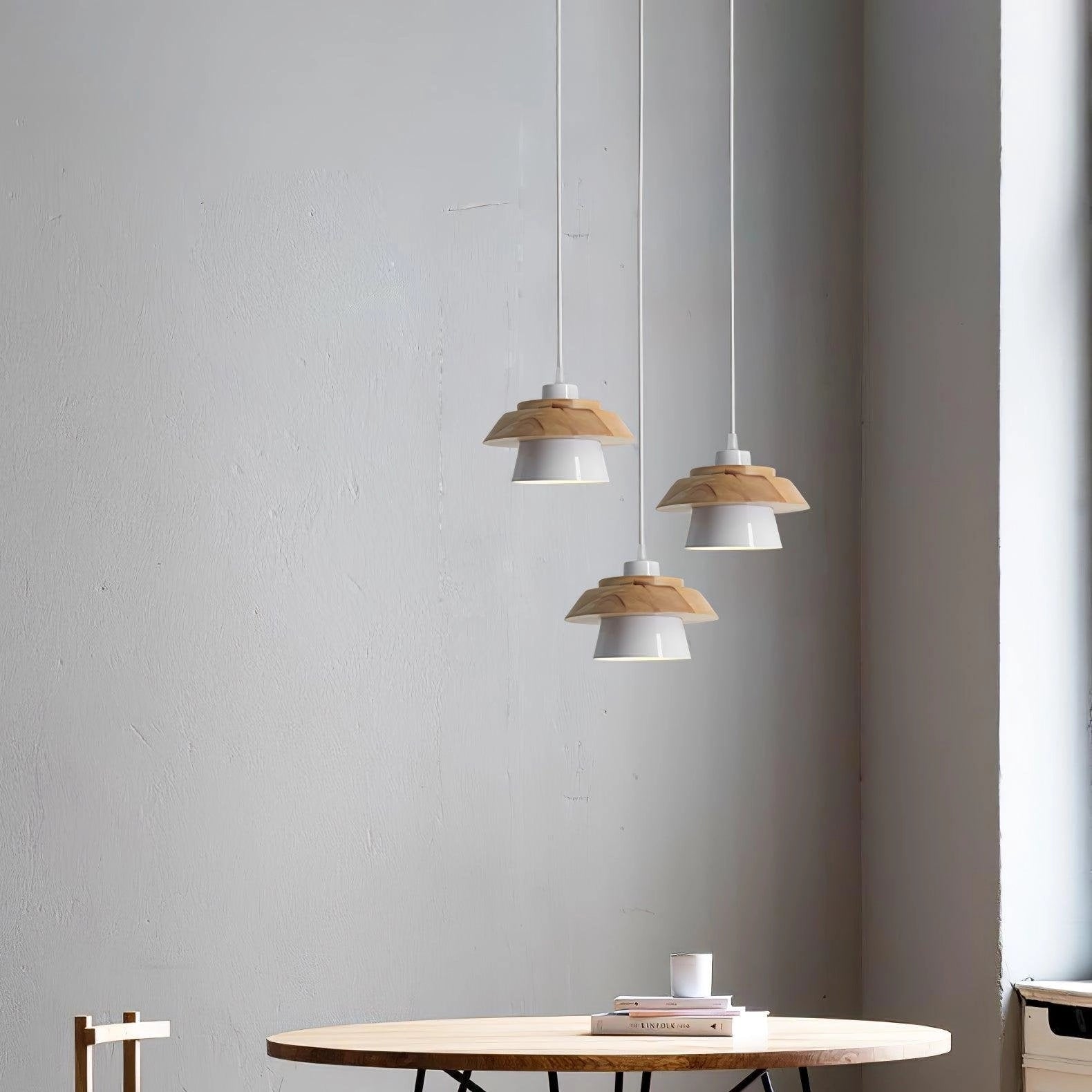 Modern Scandinavian black pendant lamp with wood accent, hanging above a table, surrounded by interior design elements including plants and a beige floor.