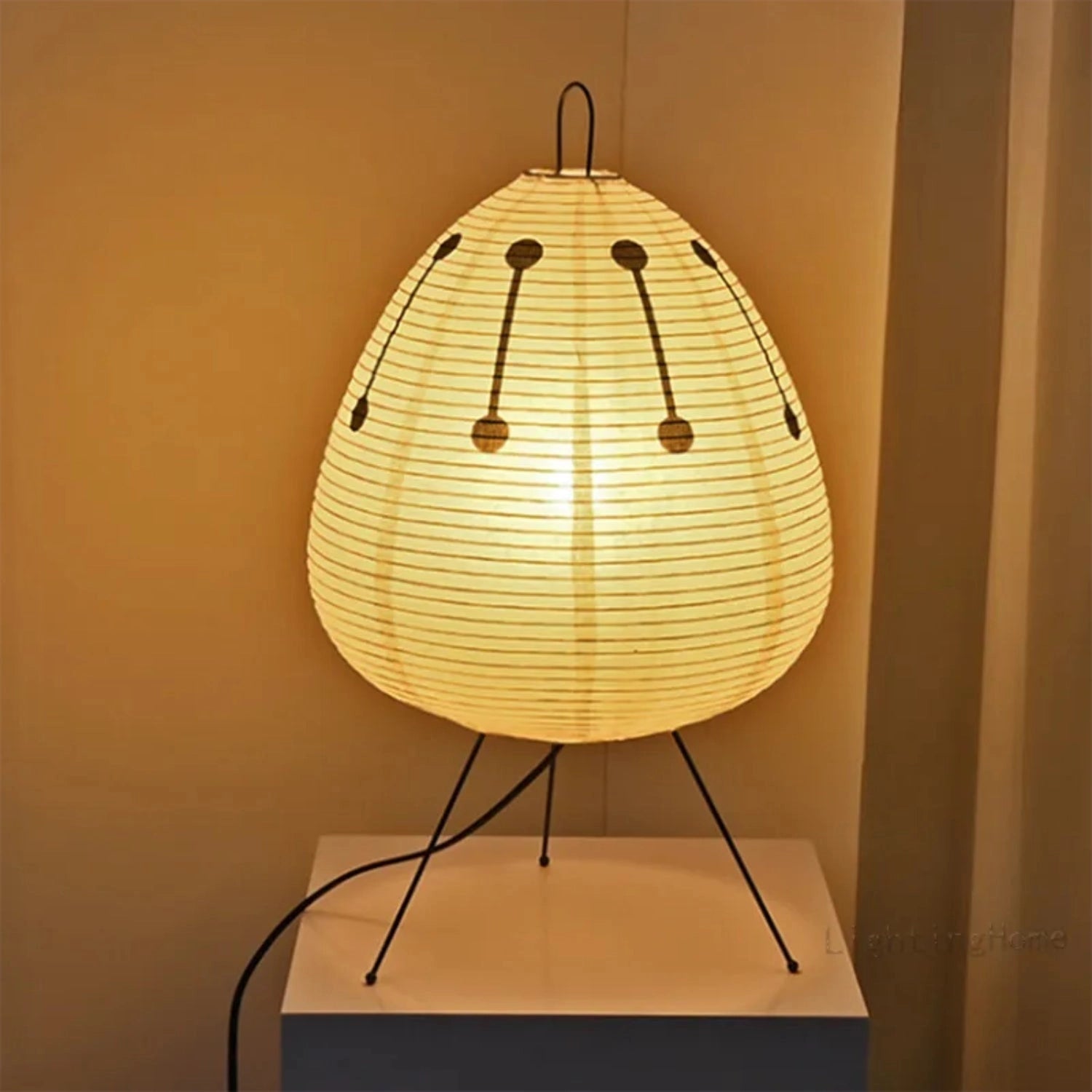 Modern tripod floor lamp with Japanese-inspired design, featuring a wooden base and a circular lampshade that emits soft ambient light, model Akari.