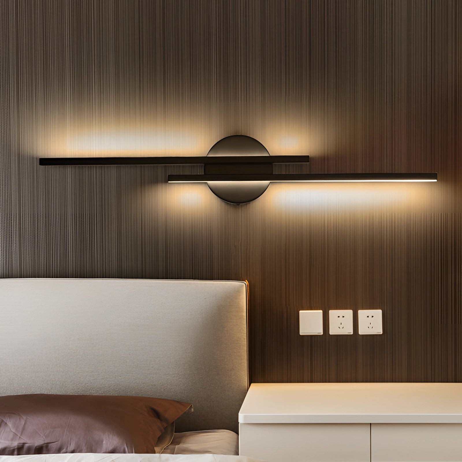 Modern vertical LED wall sconce in black with a circular minimalist design, mounted on a wooden wall in a stylish interior setting, providing ambient lighting near a brown couch and wooden flooring.